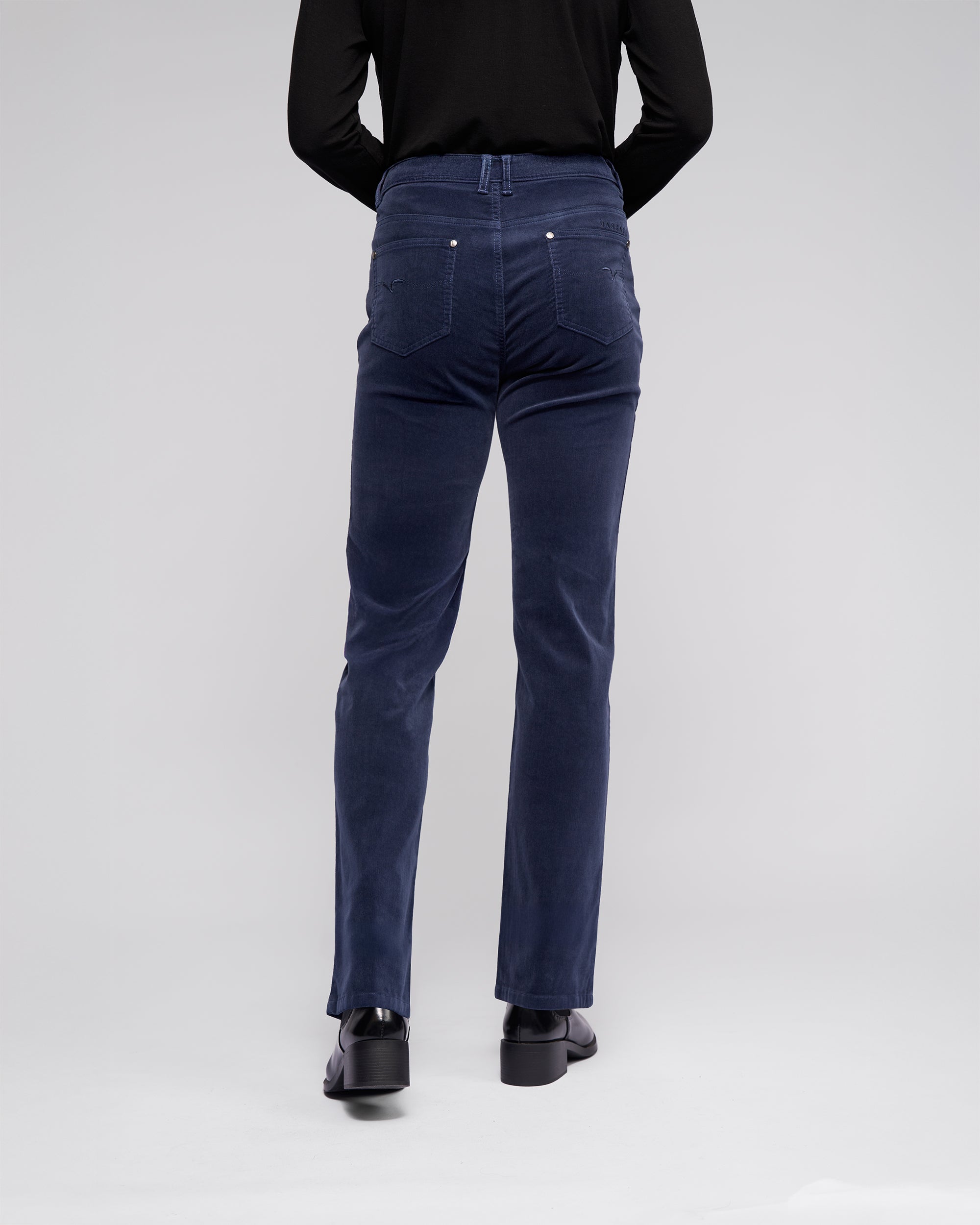 A person wearing a black long-sleeve top, dark blue high-waisted jeans, and black shoes is shown standing with their back to the camera against a plain light gray background.