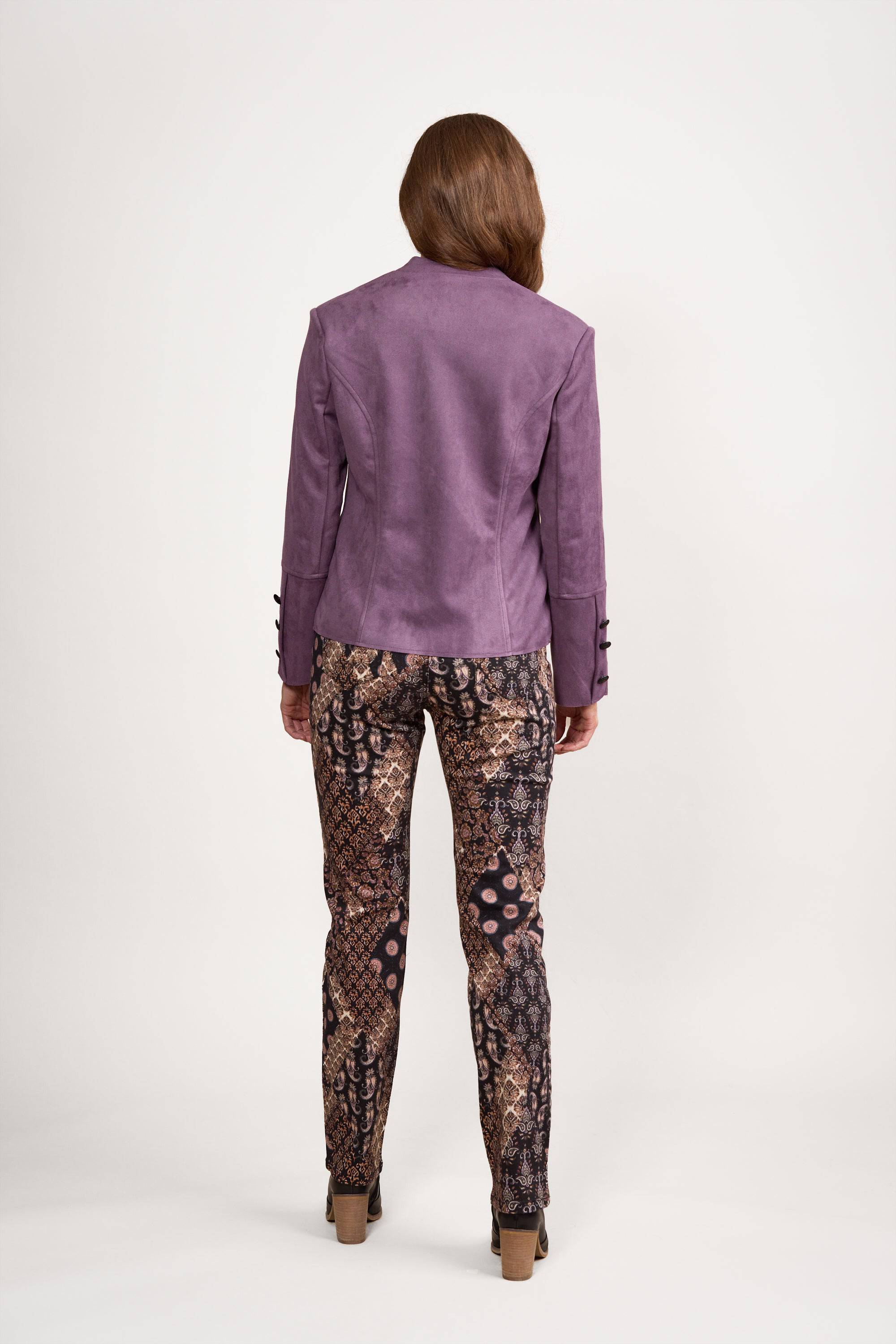 A person stands facing away, wearing the Vassalli Military Jacket in Grape with patterned pants and brown high-heeled shoes, set against a plain white background.