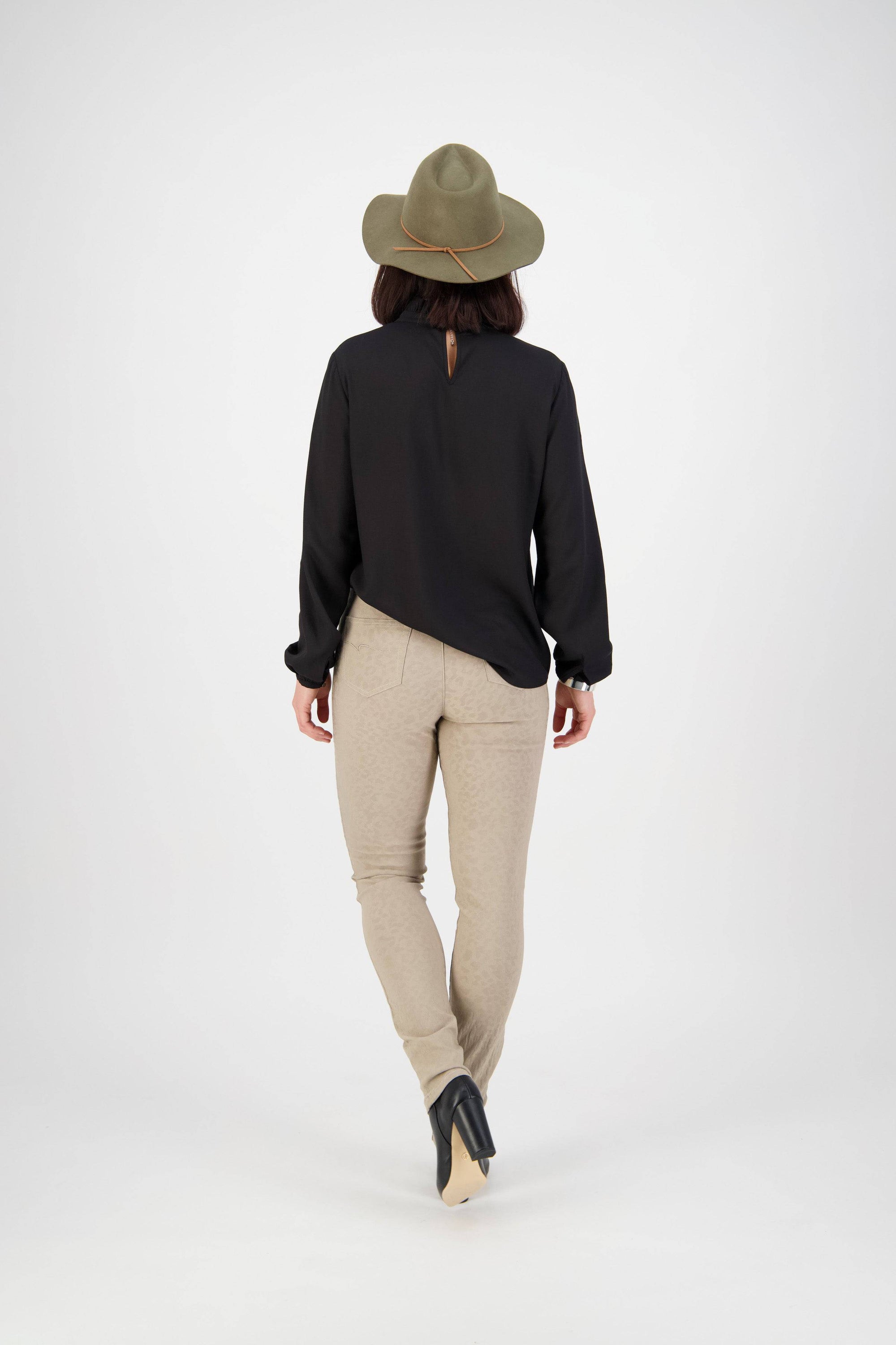 A person wearing a green wide-brimmed hat, black long-sleeve shirt, and Vassalli Origin Pull On - Taupe pants stands facing away against a plain white background.