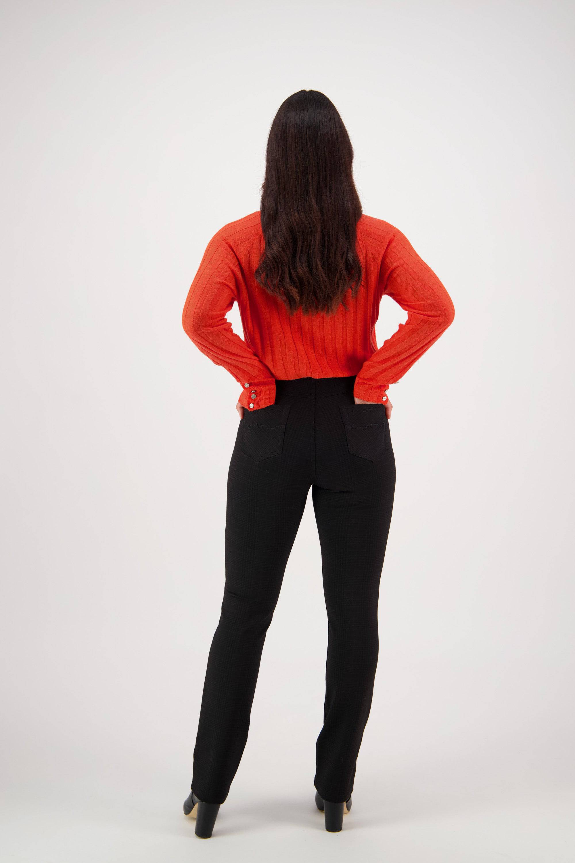 A person with long brown hair stands facing away, hands on hips, wearing a bright red long-sleeve top, Vassalli Bay Ponti Pull On - Albert pants, and black heeled shoes against a plain white background.