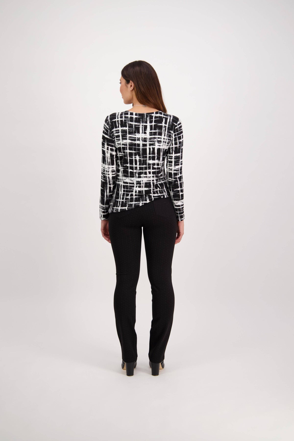 A woman faces away with brown hair down, wearing a black-and-white patterned long-sleeve top and Vassalli Bay Ponti Pull On - Colombia pants, set against a plain light background.