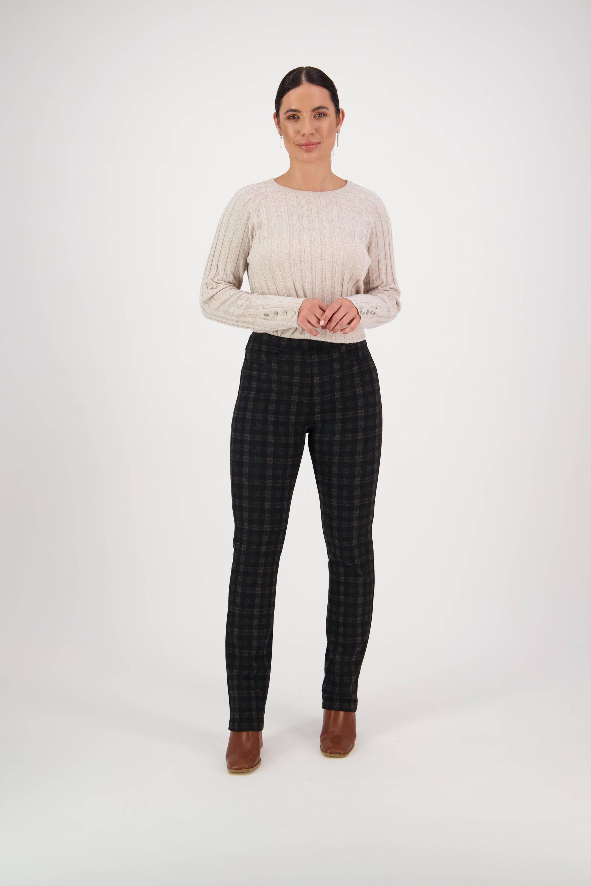 A woman stands before a white background wearing a cream knit sweater, brown ankle boots, and Vassalli's Bay Ponti Pull On - Halifax pants. Her hands are lightly clasped as she looks forward with a slight smile.