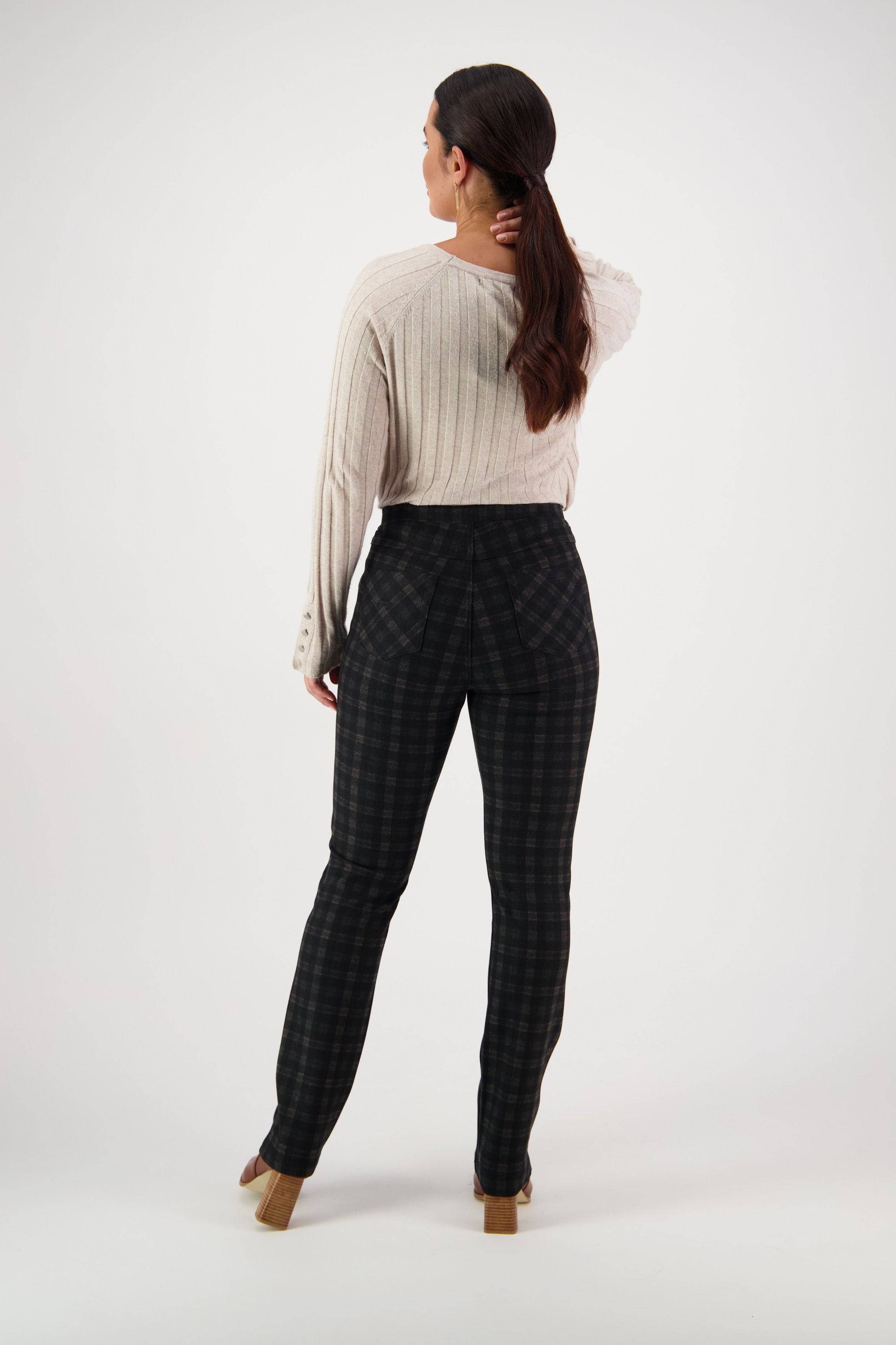 A woman stands facing away, holding her long dark hair. She wears a beige ribbed sweater and Vassalli Bay Ponti Pull On - Halifax pants with heeled shoes, set against a plain white background.