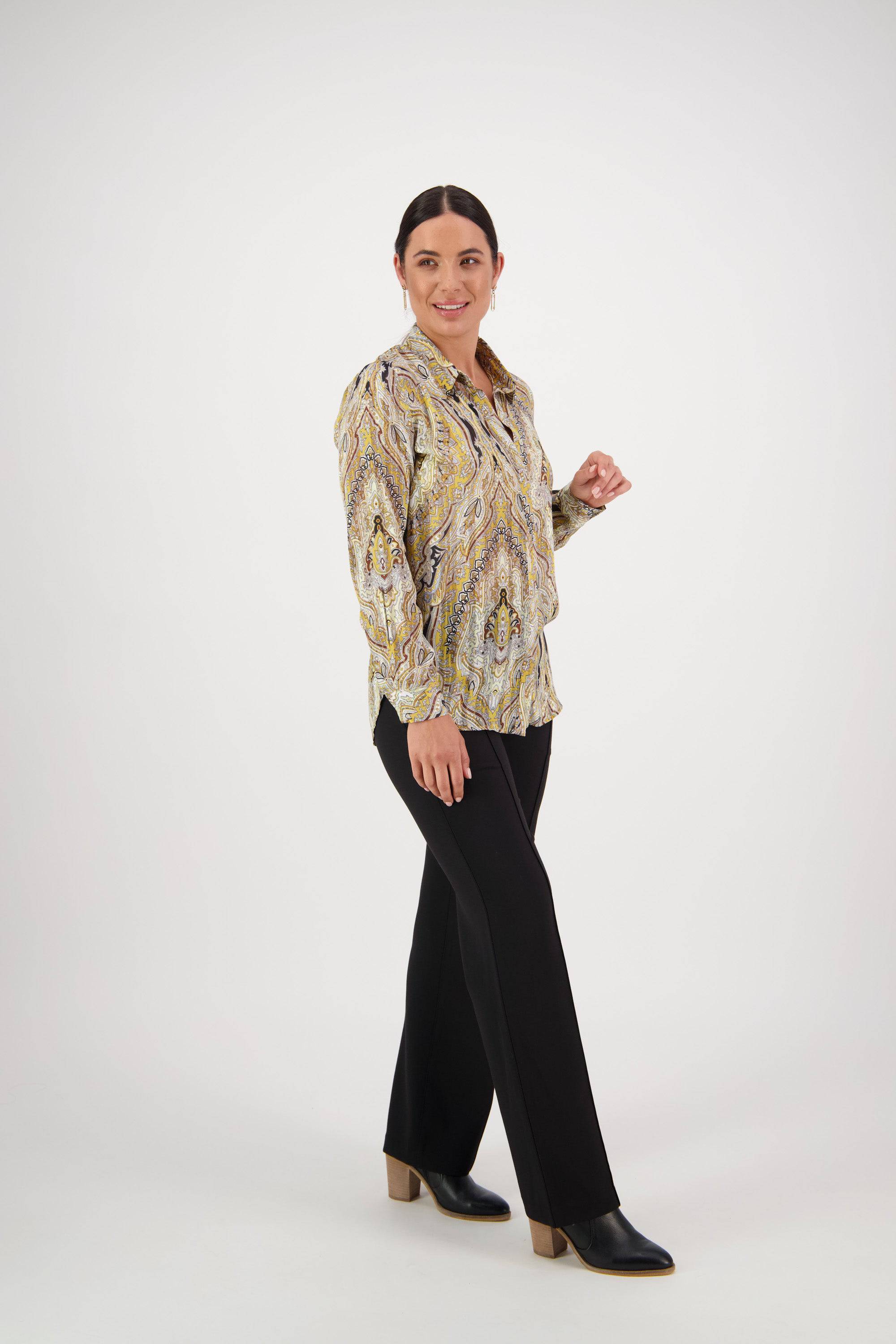 A woman models the Vassalli Ballot Shirt - Majestic, with semi-sheer fabric and gold lurex stripes. She poses confidently against a white background, smiling with her dark hair back, paired with black pants and heeled ankle boots.