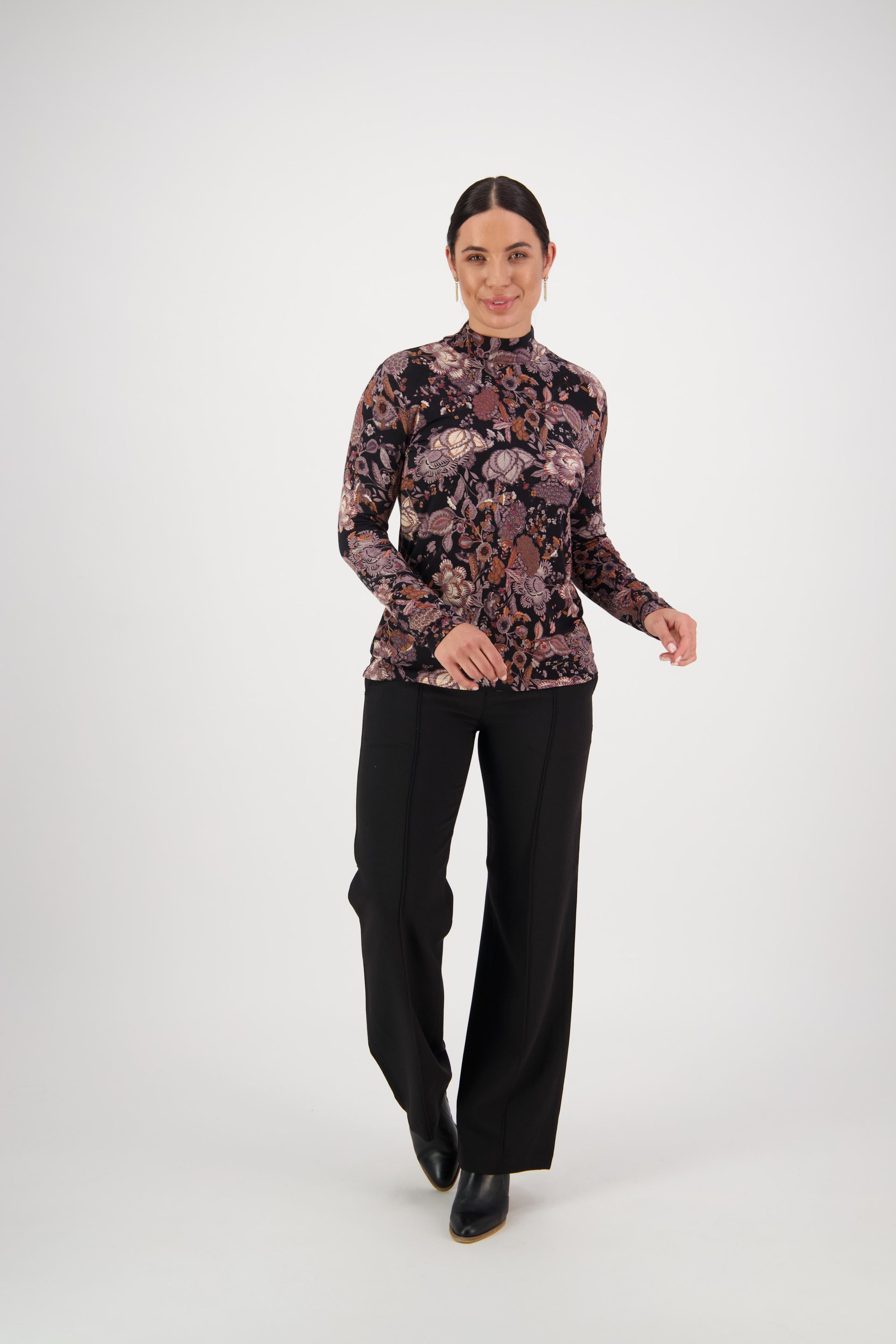 A woman with dark hair in a low ponytail smiles with her hands slightly raised, wearing the Vassalli Foundation Top - Vintage, black wide-leg pants, and black shoes against a plain white background.