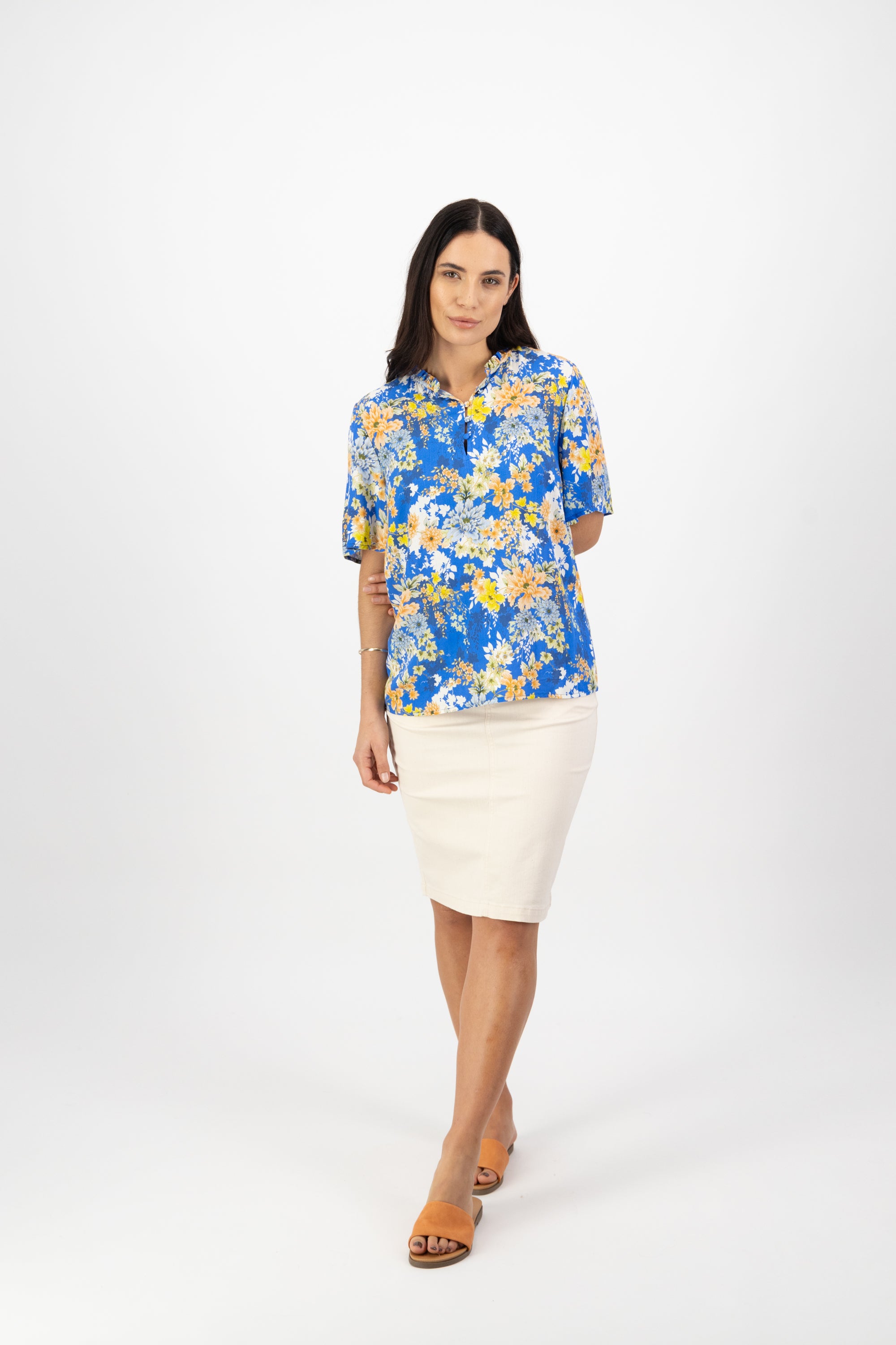 A woman with long dark hair wears the Vassalli Floaty Sleeve Top - Kimono Dream, paired with a white knee-length skirt and tan sandals, standing against a plain white background.