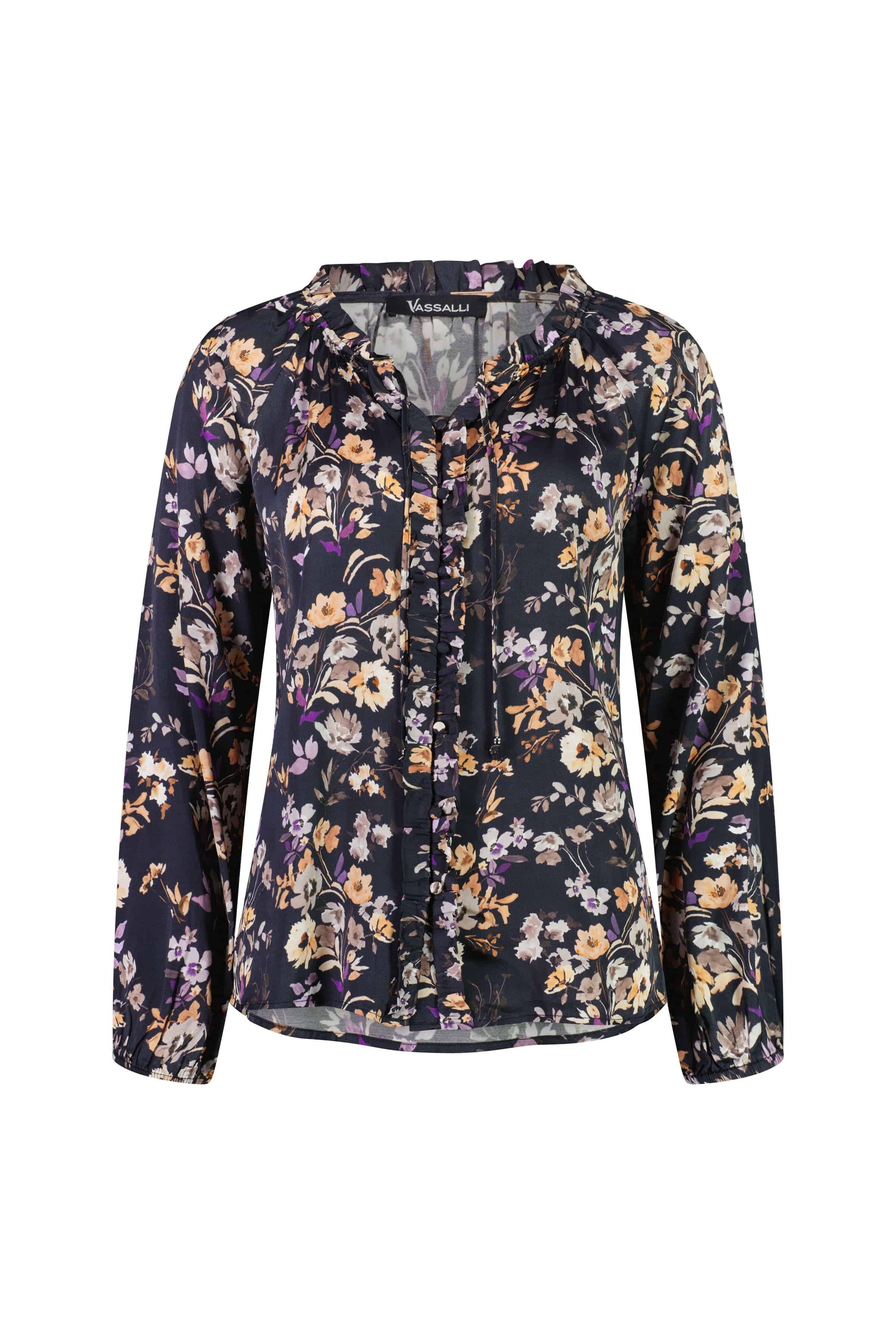 The Vassalli V-Neck Top - Flora features long sleeves, a ruffled collar, and a floral print in white, yellow, and purple on a dark background. The inner label displays the Vassalli brand.