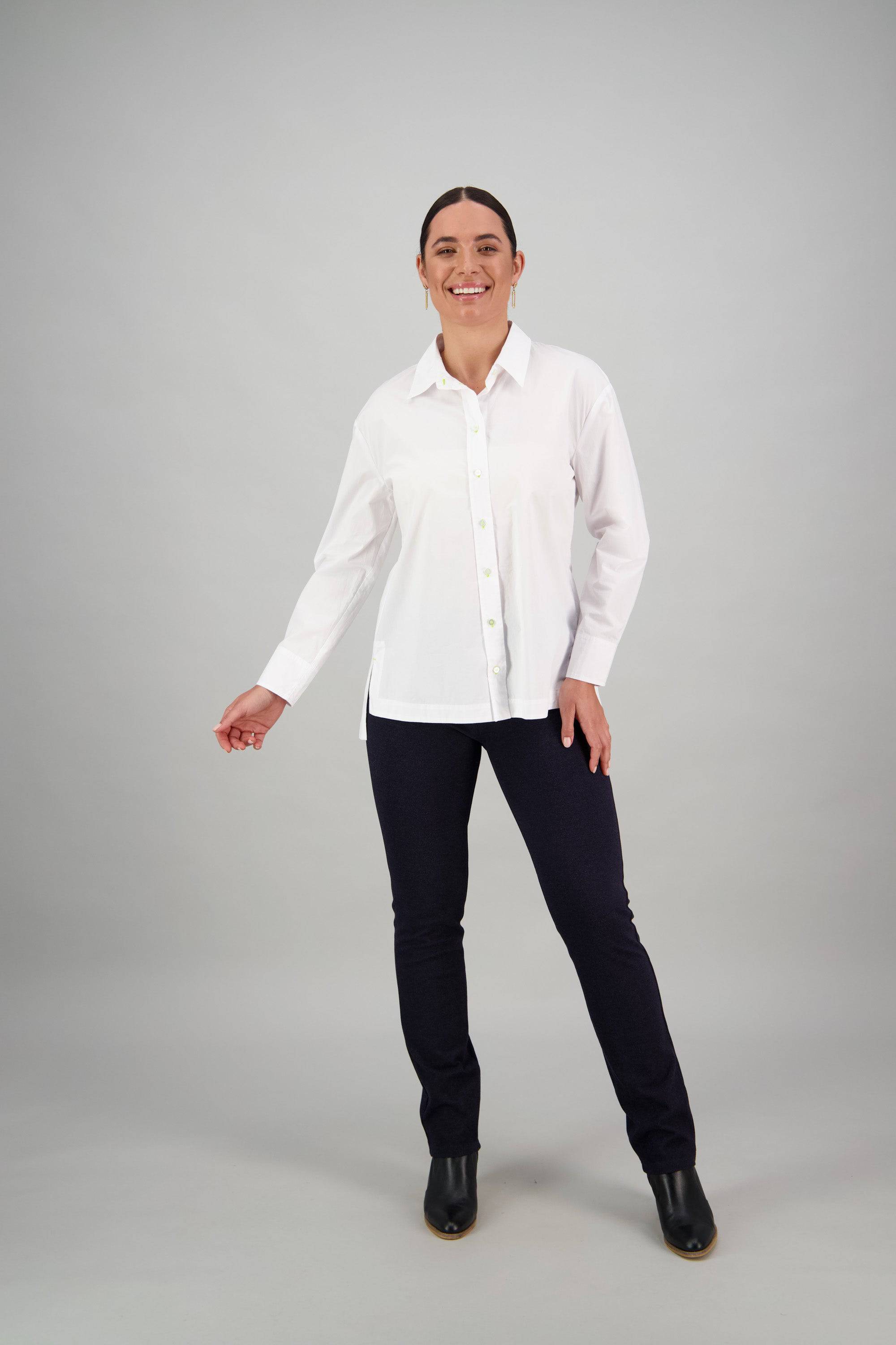 A person stands and smiles, dressed in a Vassalli Shirt - White/Lime, paired with dark pants and black boots, set against a plain light gray background.