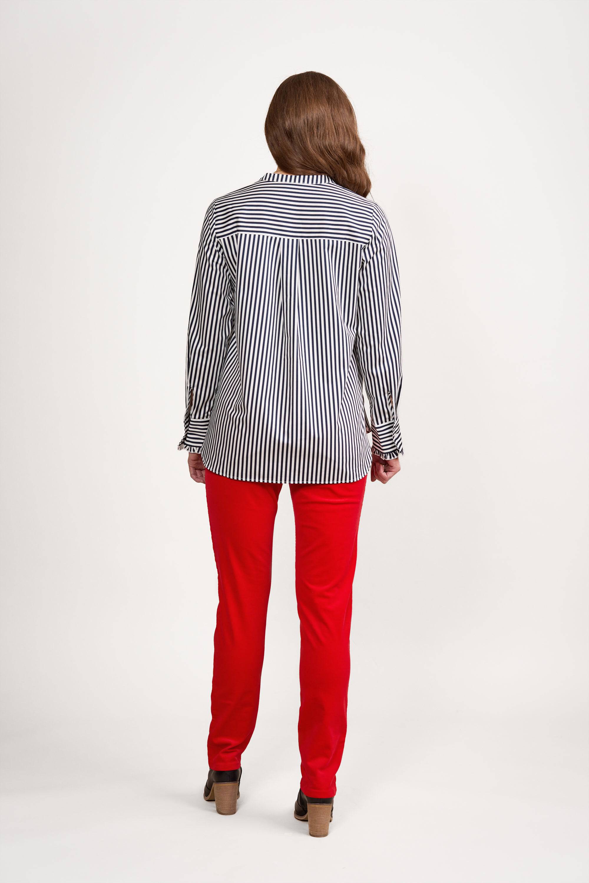 Wearing the Vassalli Manhattan Shirt in Ink/White, a person with long brown hair stands facing away against a plain white background, styled with bright red pants and brown heeled shoes.