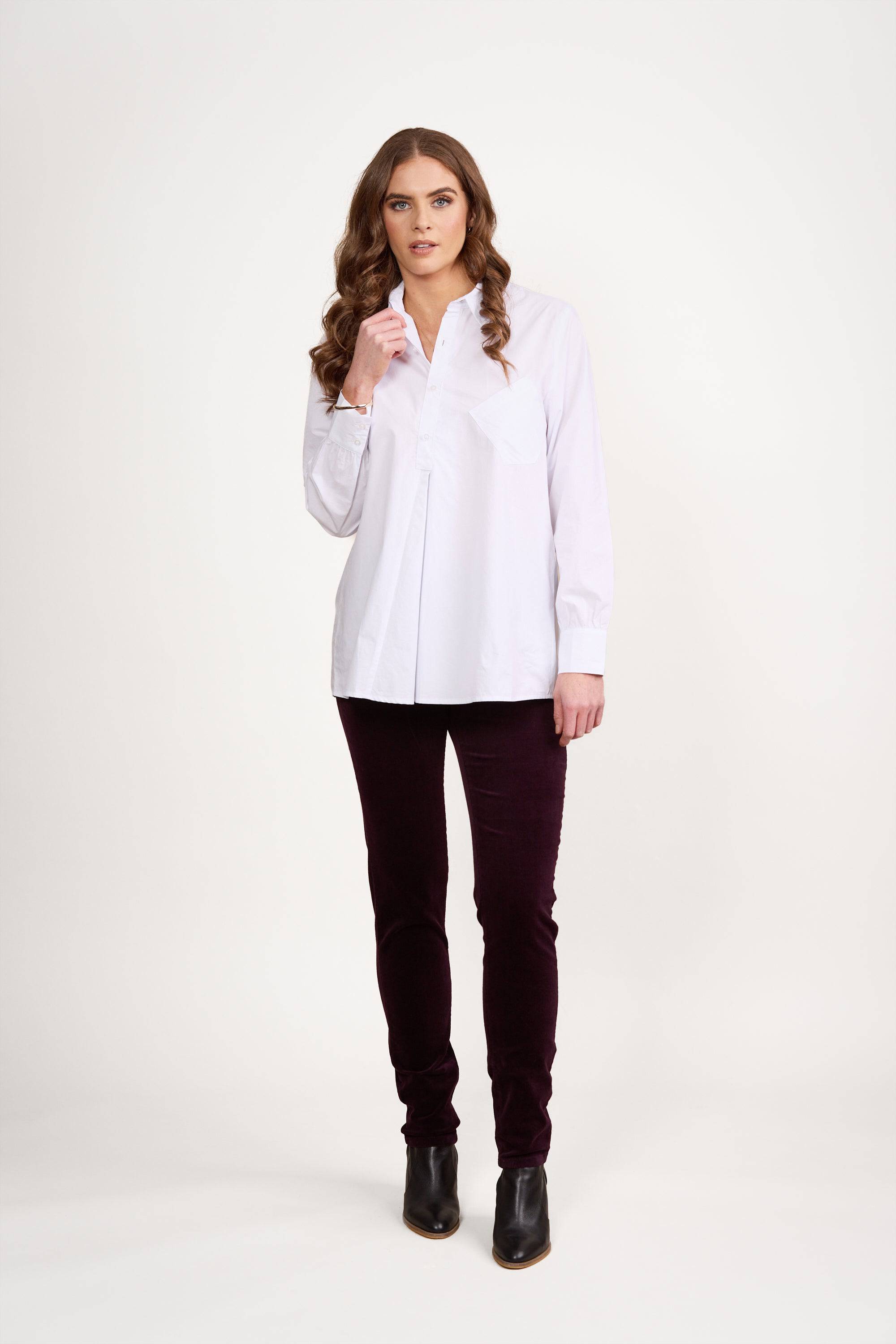 A woman with long brown hair wears the Vassalli Half Placket Shirt in white, styled with dark pants and black ankle boots, standing against a plain white background.