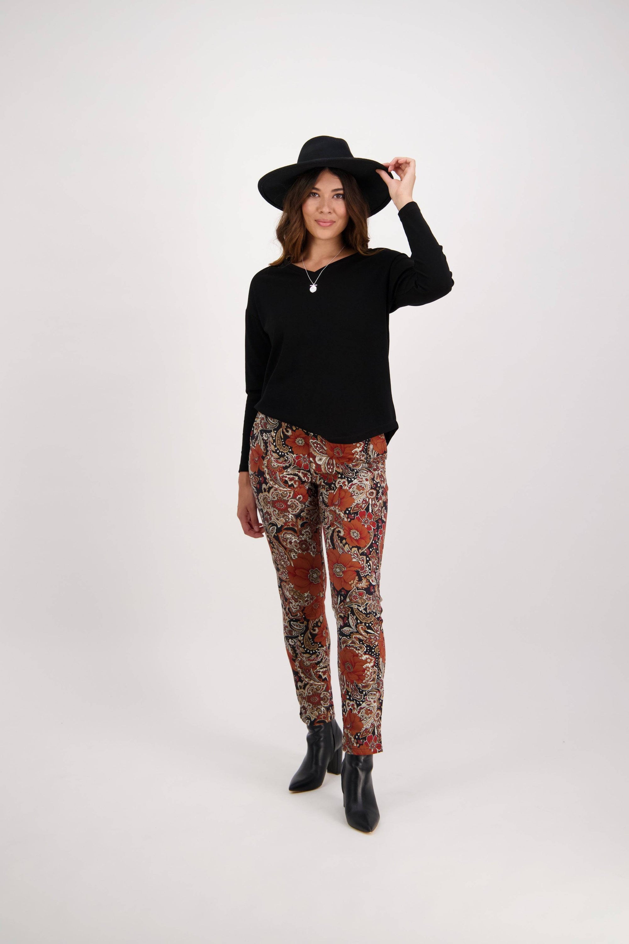 Woman wearing a black hat, black long-sleeve top, Vassalli Ankle Grazer Pant - Bohemian, and black ankle boots stands against a plain white background.