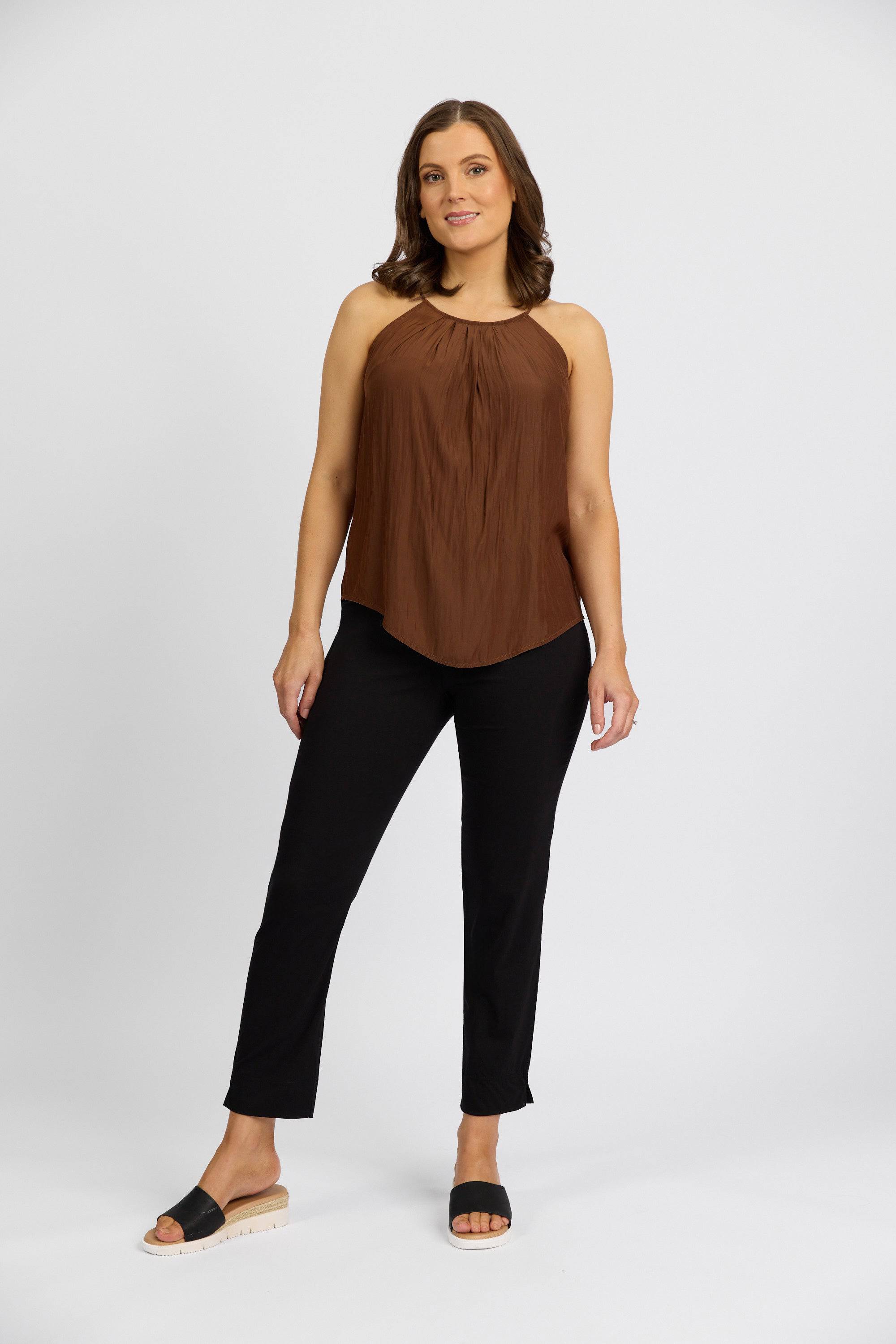 A woman with shoulder-length brown hair smiles slightly, wearing a sleeveless brown top and Vassalli Paris Capri Pant in Black, paired with black slide sandals against a plain white background.