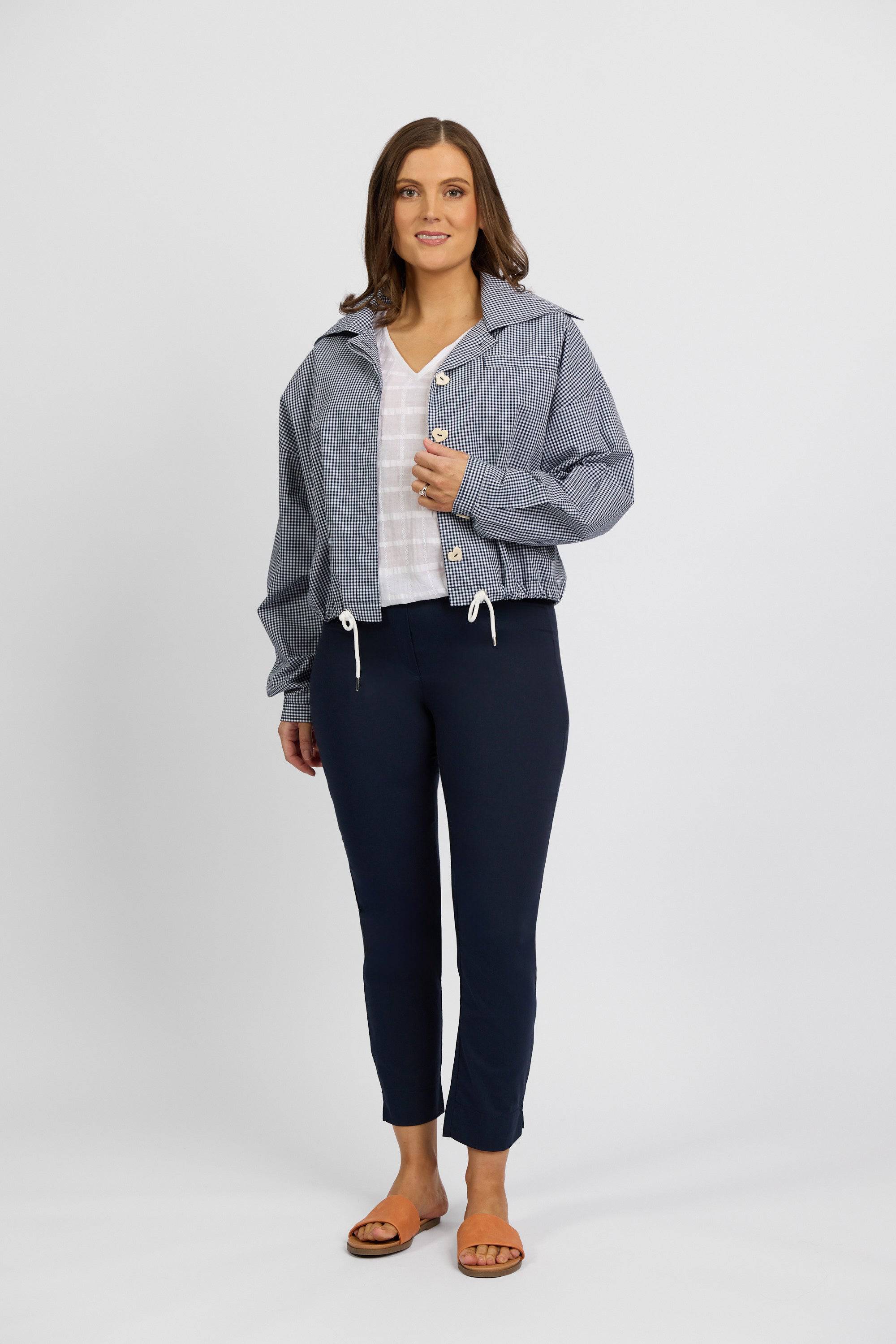 A woman smiles in a blue and white striped jacket over a white top, wearing Vassalli Paris Capri Pant - Inka and brown sandals, against a plain light gray background.