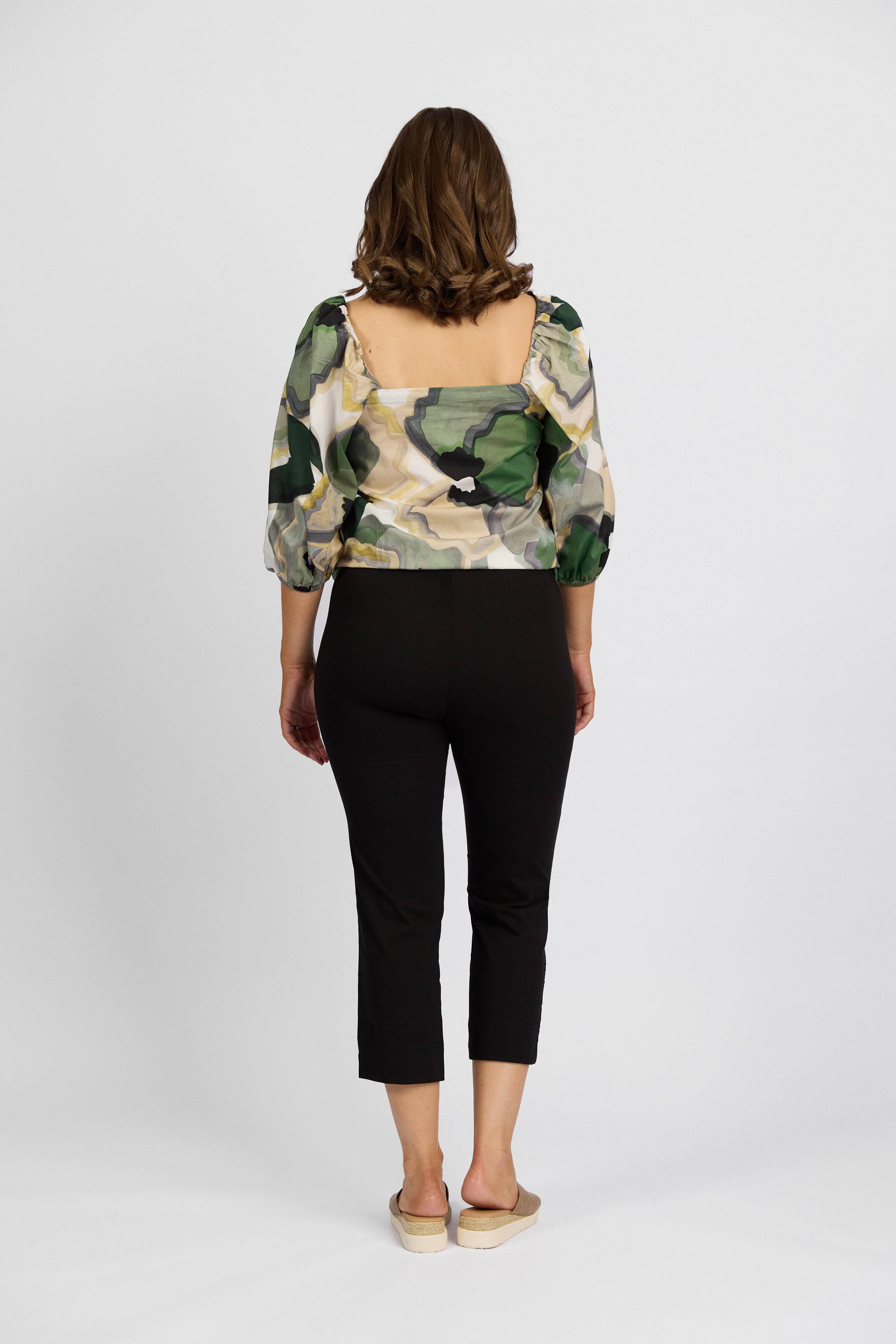 A woman faces away from the camera, wearing a green camouflage Paris Crop top, Vassalli Paris Crop Pant - Black, and beige slip-on shoes against a plain white background.