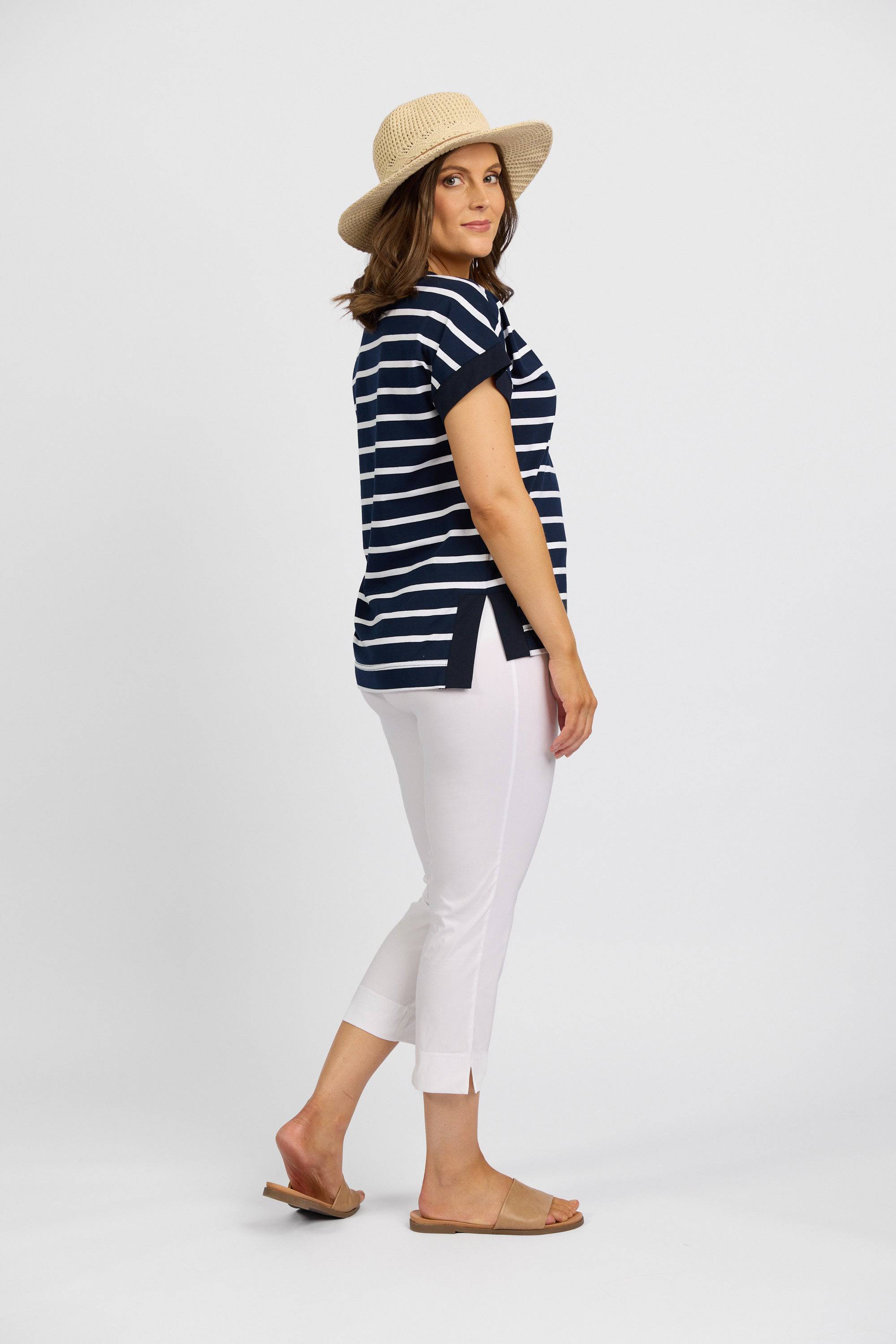 A woman stands sideways against a white background, wearing a straw hat, navy and white striped short-sleeve shirt, Vassalli Paris Crop Pant - White, and tan sandals.