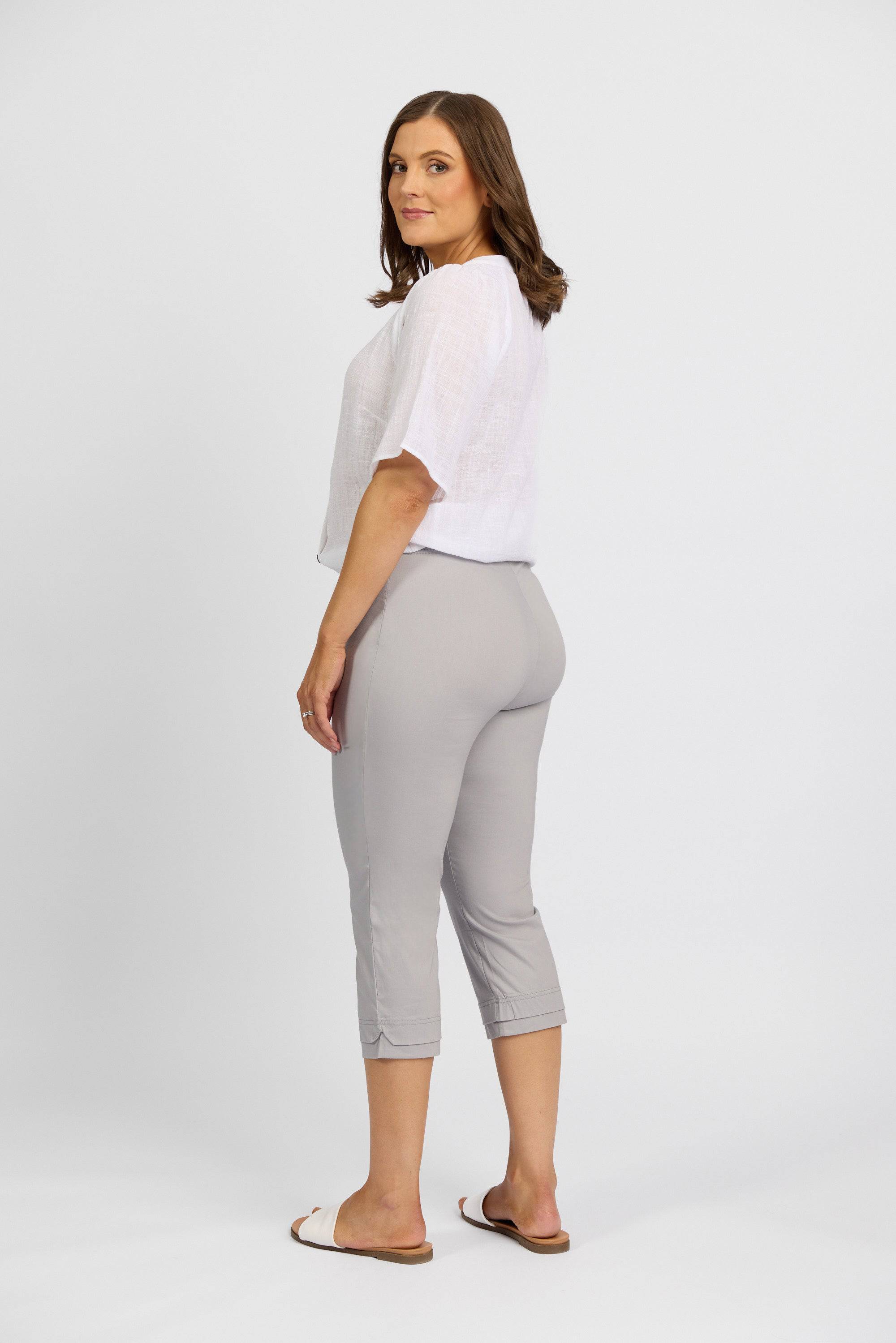A woman with shoulder-length brown hair models the Vassalli Paris 3/4 Pant in Silver, styled with a loose white top and white sandals, standing sideways and looking at the camera against a plain white background.