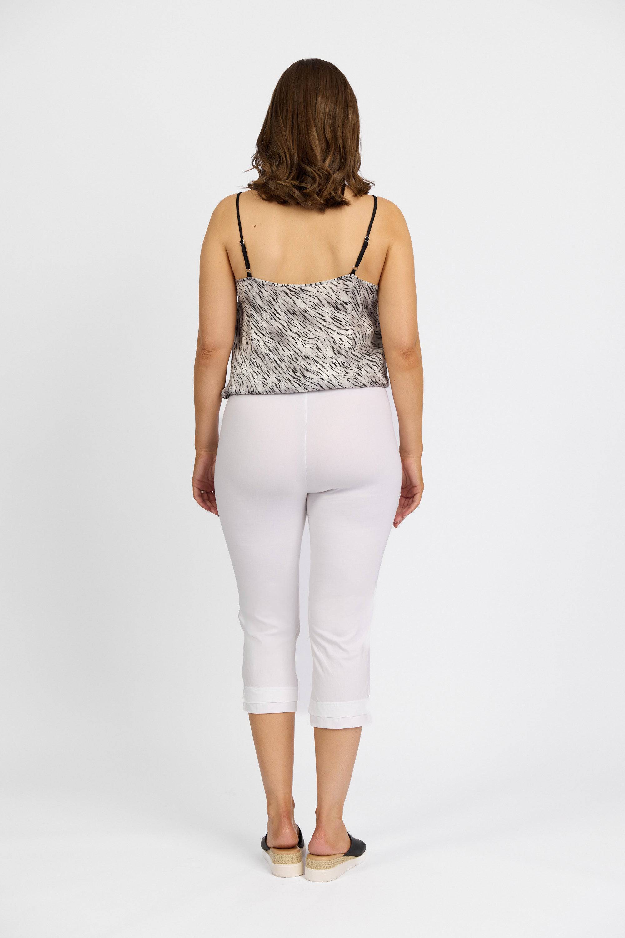 A woman faces away from the camera wearing a sleeveless patterned top, black slip-on shoes, and Vassalli Paris 3/4 Pant in white against a plain white background.