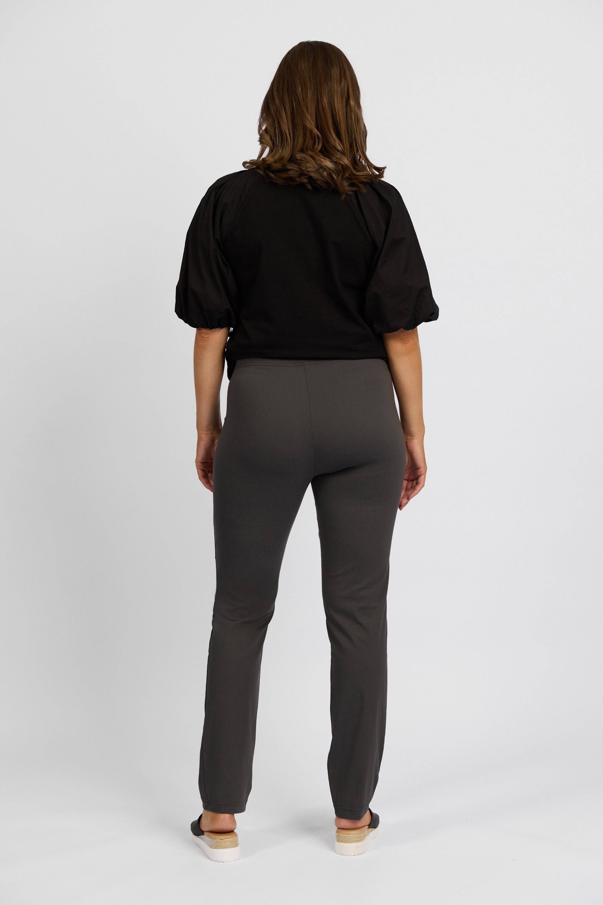 A person with shoulder-length brown hair, seen from the back, wears a black short-sleeve top and Vassalli's Paris Full Length Pant - Beluga, paired with beige shoes, set against a plain white background.