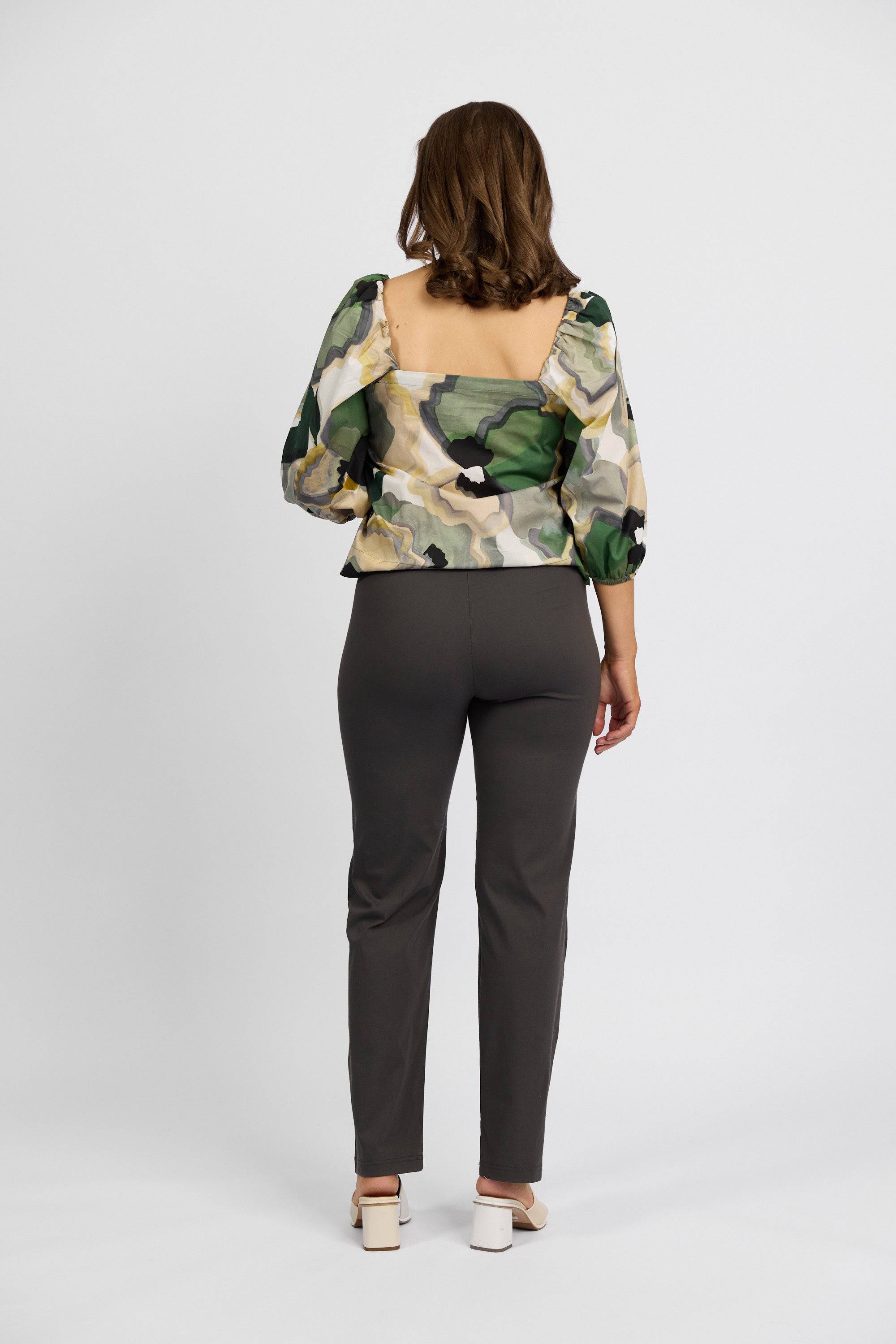A woman faces away, wearing a sheer green, white, and yellow blouse with puffed sleeves, Vassalli Paris Full Length Pant - Beluga, and light block-heeled sandals against a plain white background.