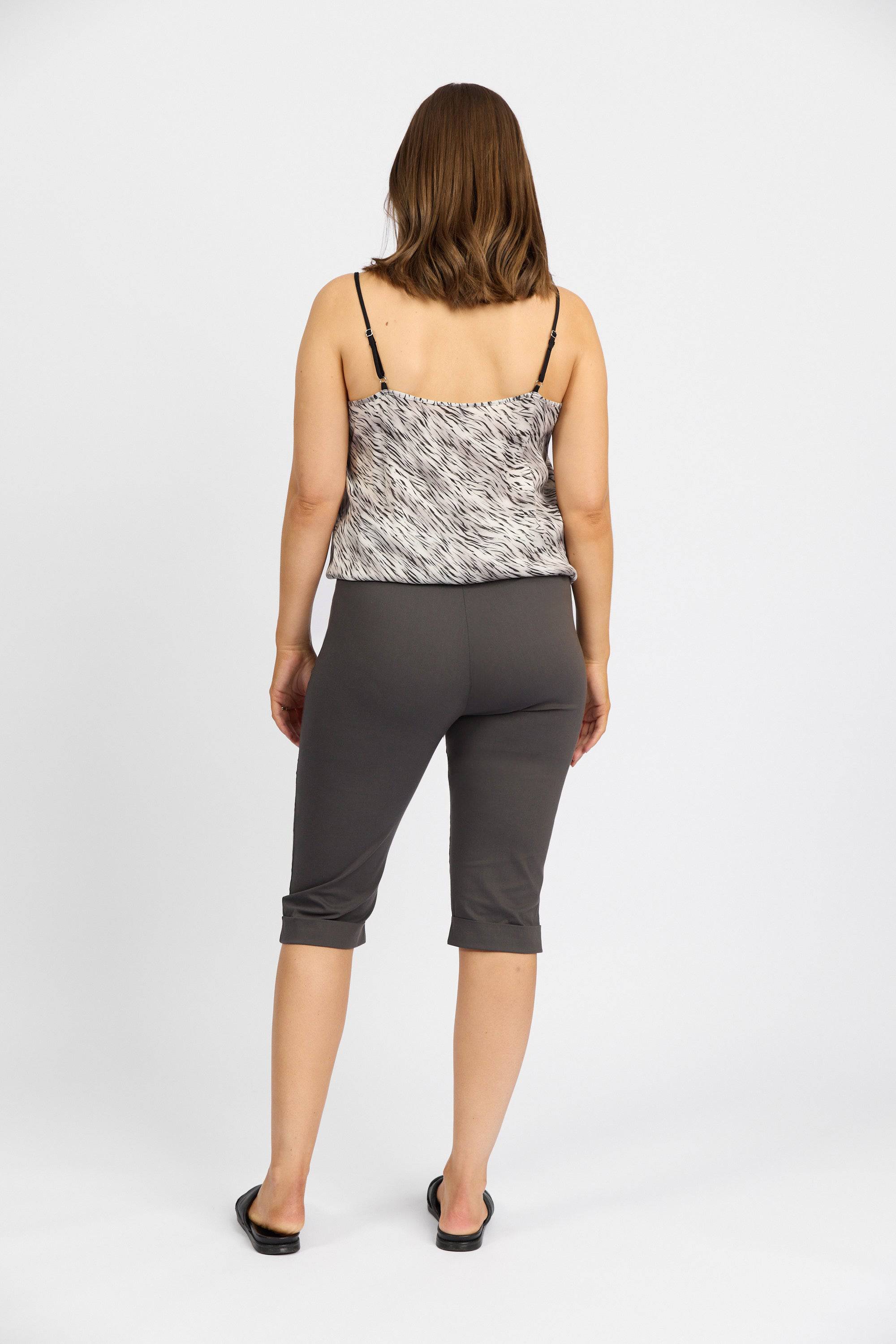 A woman faces away from the camera, wearing a patterned sleeveless top, black sandals, and Vassalli Paris Short - Beluga mid-rise capris, against a plain white background.
