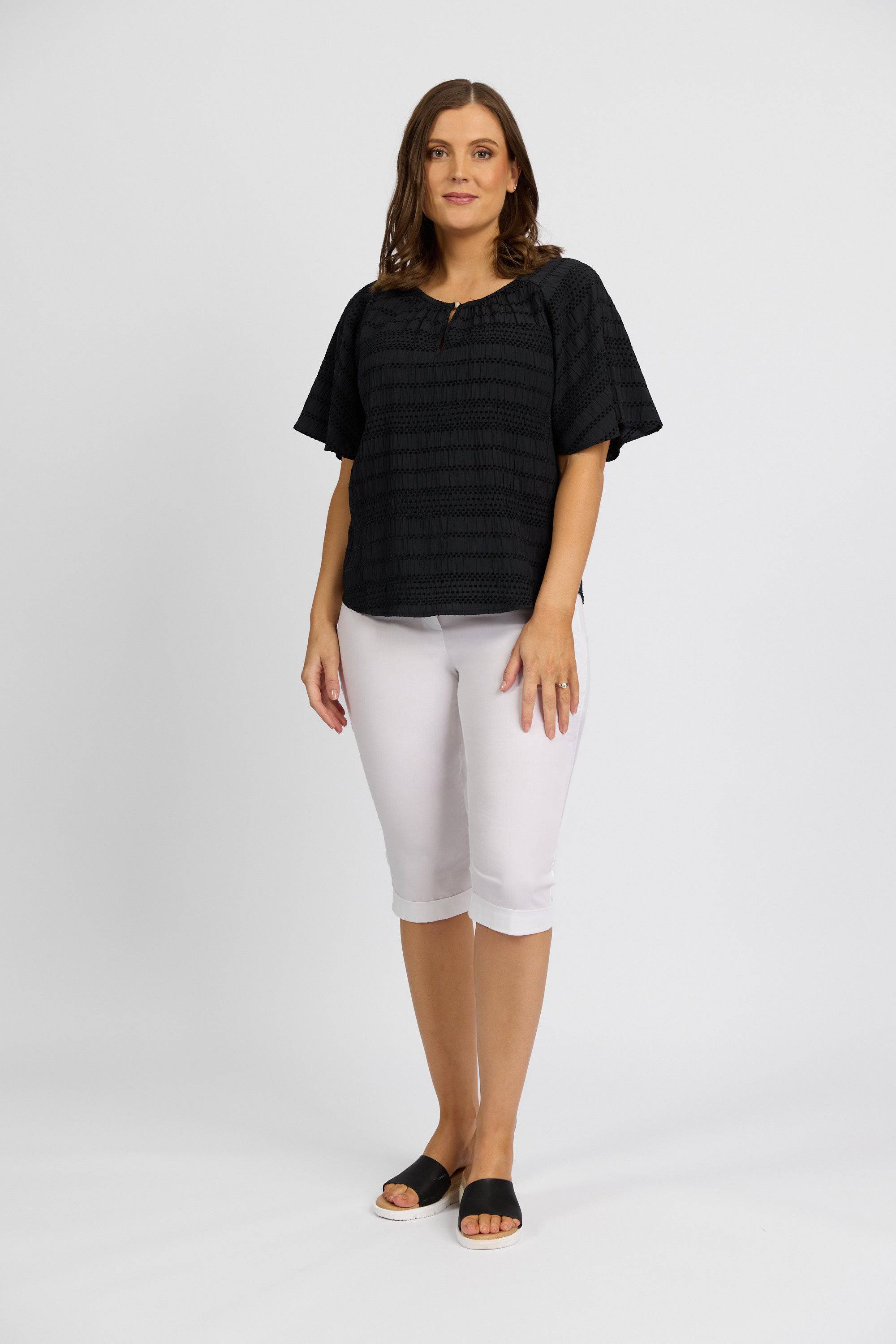 A woman with shoulder-length brown hair wears the Vassalli Paris Short in white and a black stretch top, styled with black slide sandals, against a plain white background. She faces the camera with a neutral expression.