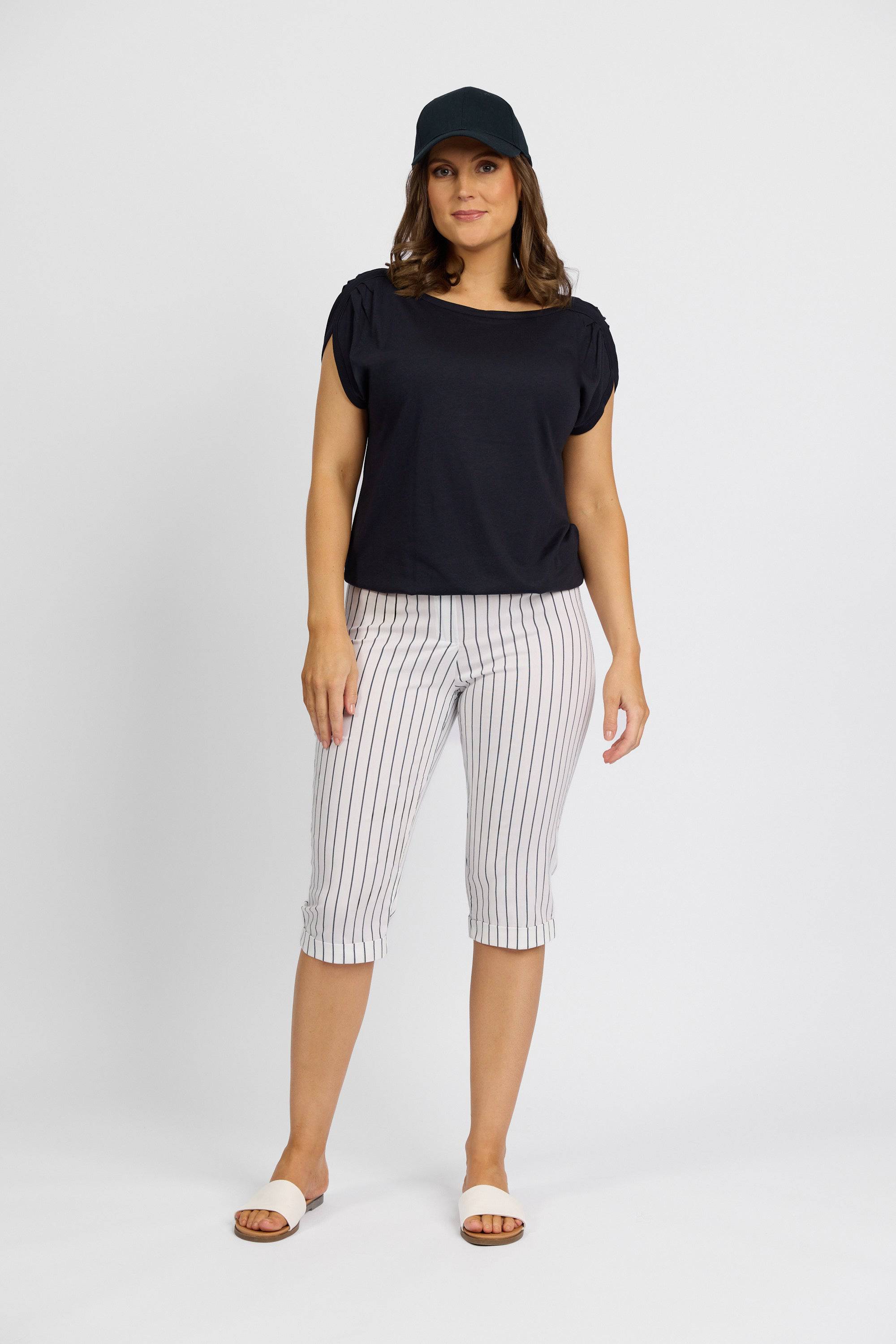 A woman stands facing the camera against a plain white background, wearing a black cap, black short-sleeved top, and Vassalli's Paris Printed Short in white with stripes.