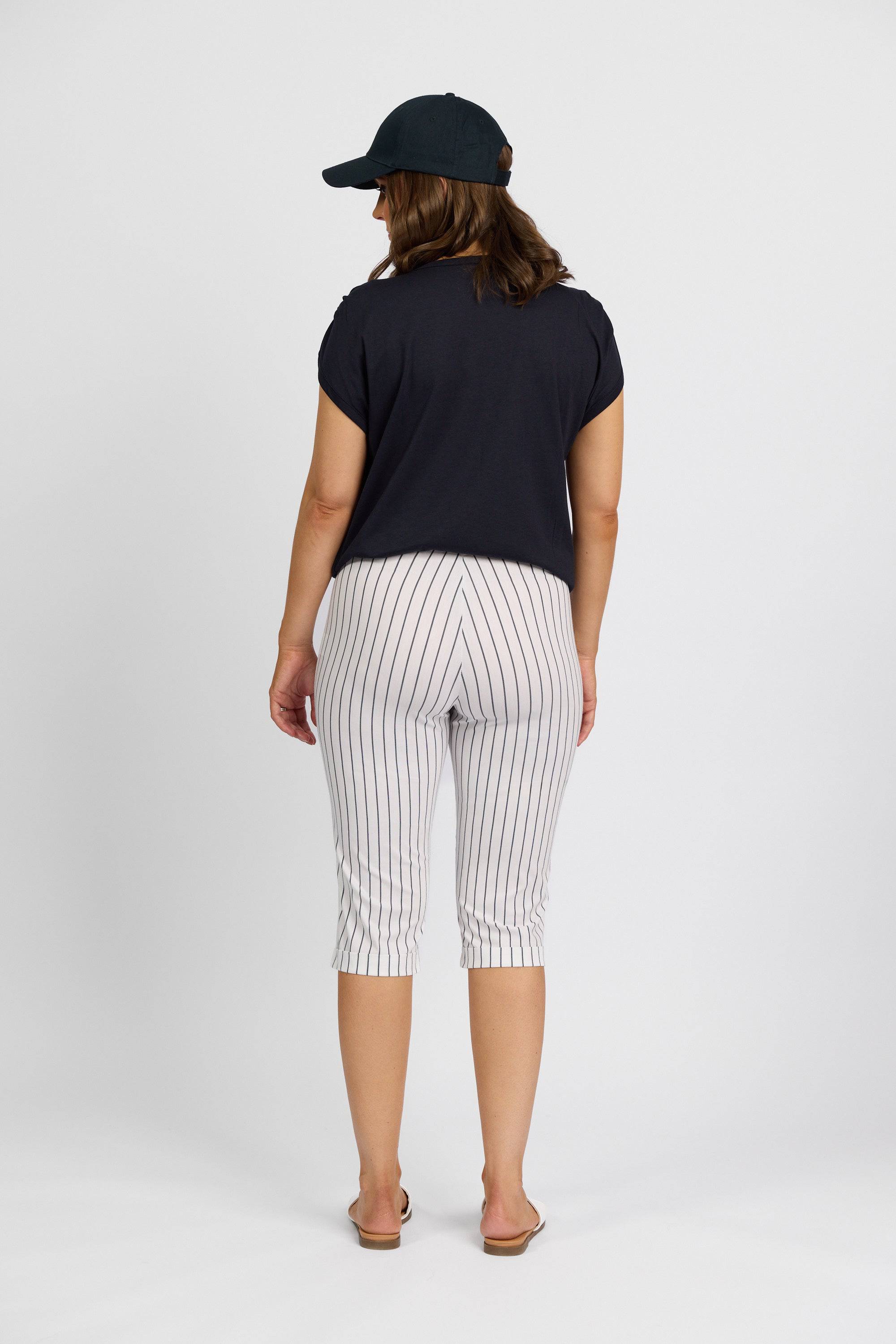 A person stands facing away, wearing a black cap, black short-sleeve shirt, and Vassalli Paris Printed Short in white with stripes, plus flip-flops, against a plain white background.