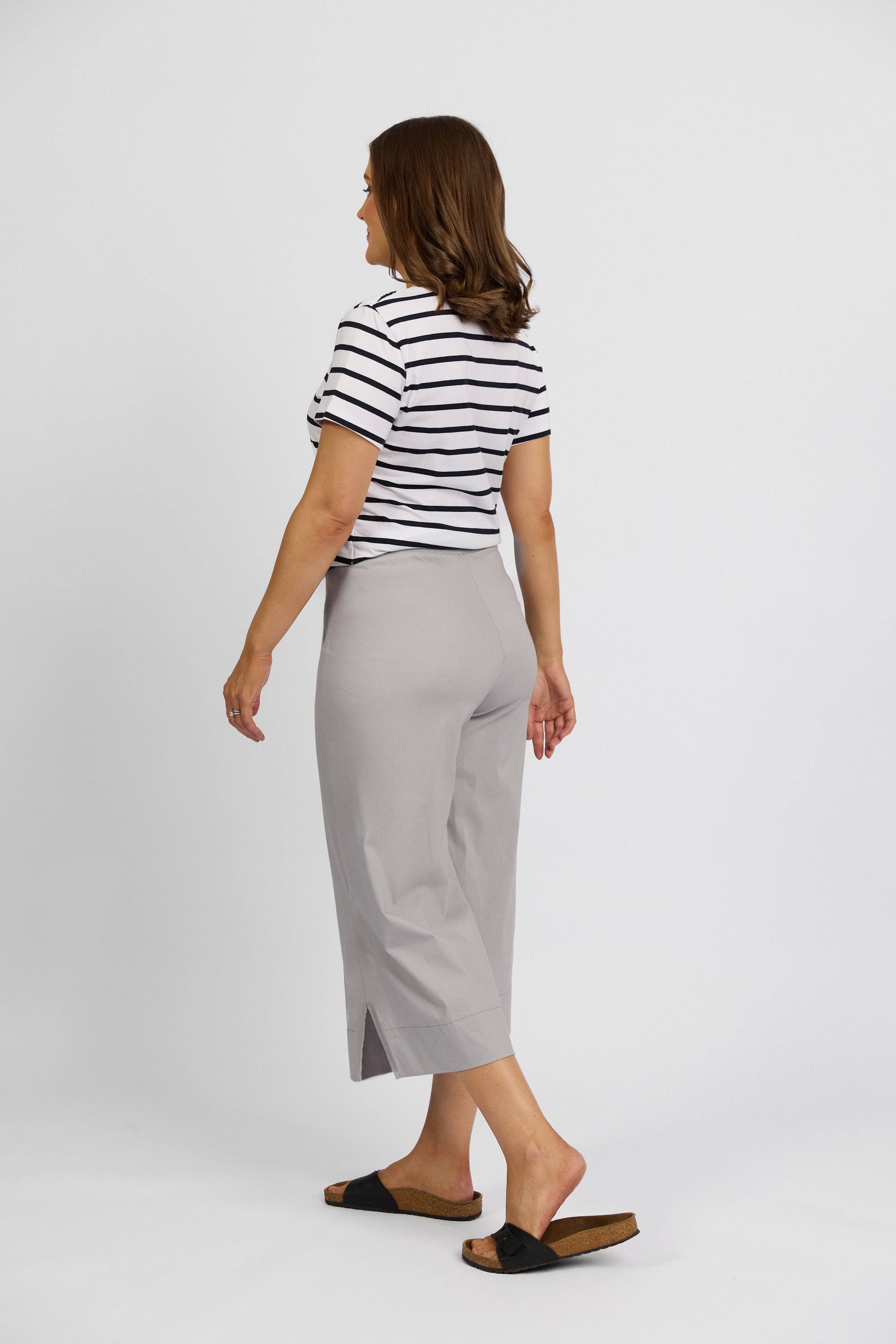 A woman with shoulder-length brown hair stands facing away against a white background, wearing a black-and-white striped short-sleeve top, Vassalli Paris Wide Leg Crop pants in Silver, and black slide sandals.