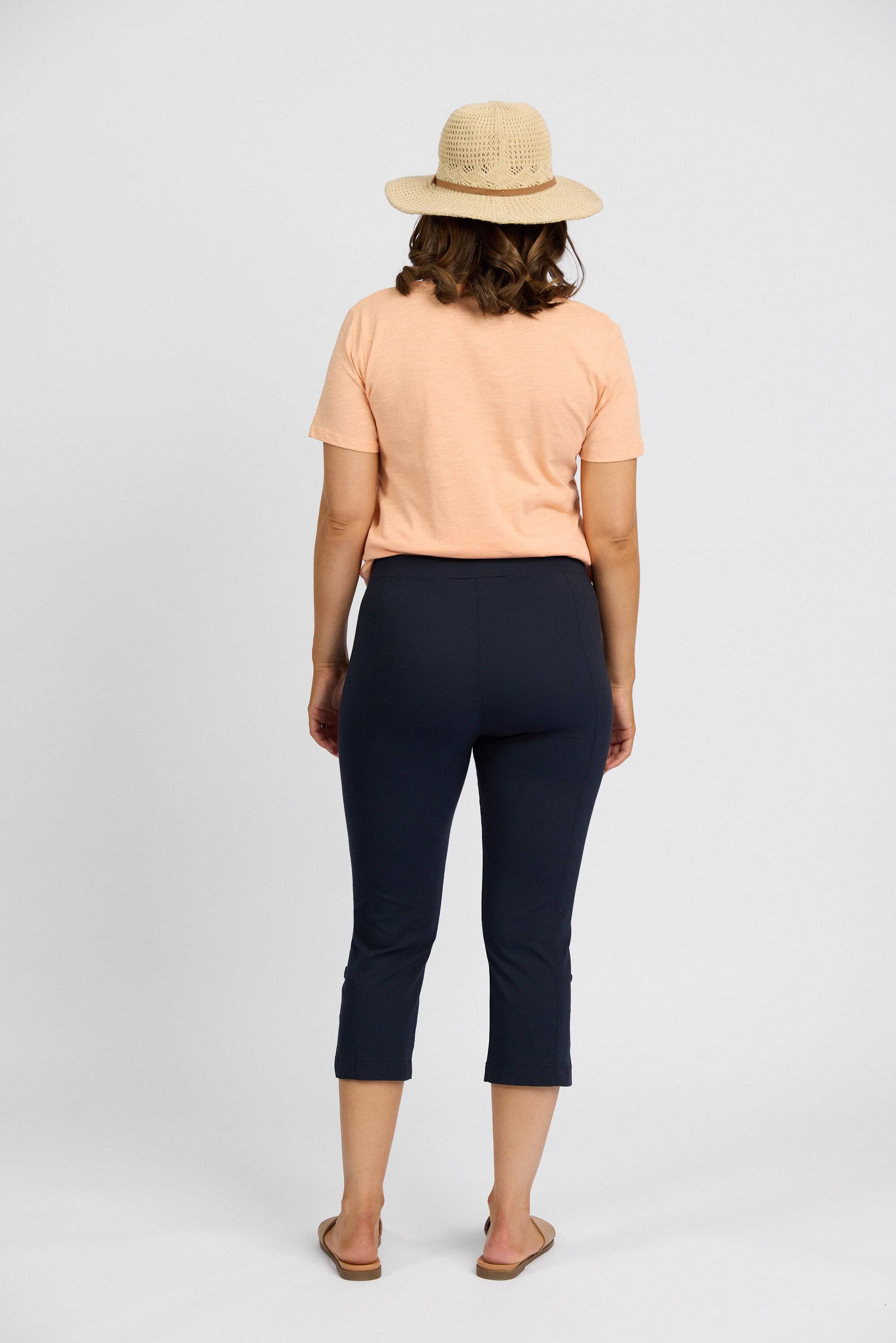 A woman in a straw hat, peach T-shirt, Vassalli Paris 3/4 Cargo Short - Inka, and sandals stands facing away from the camera against a plain white background.
