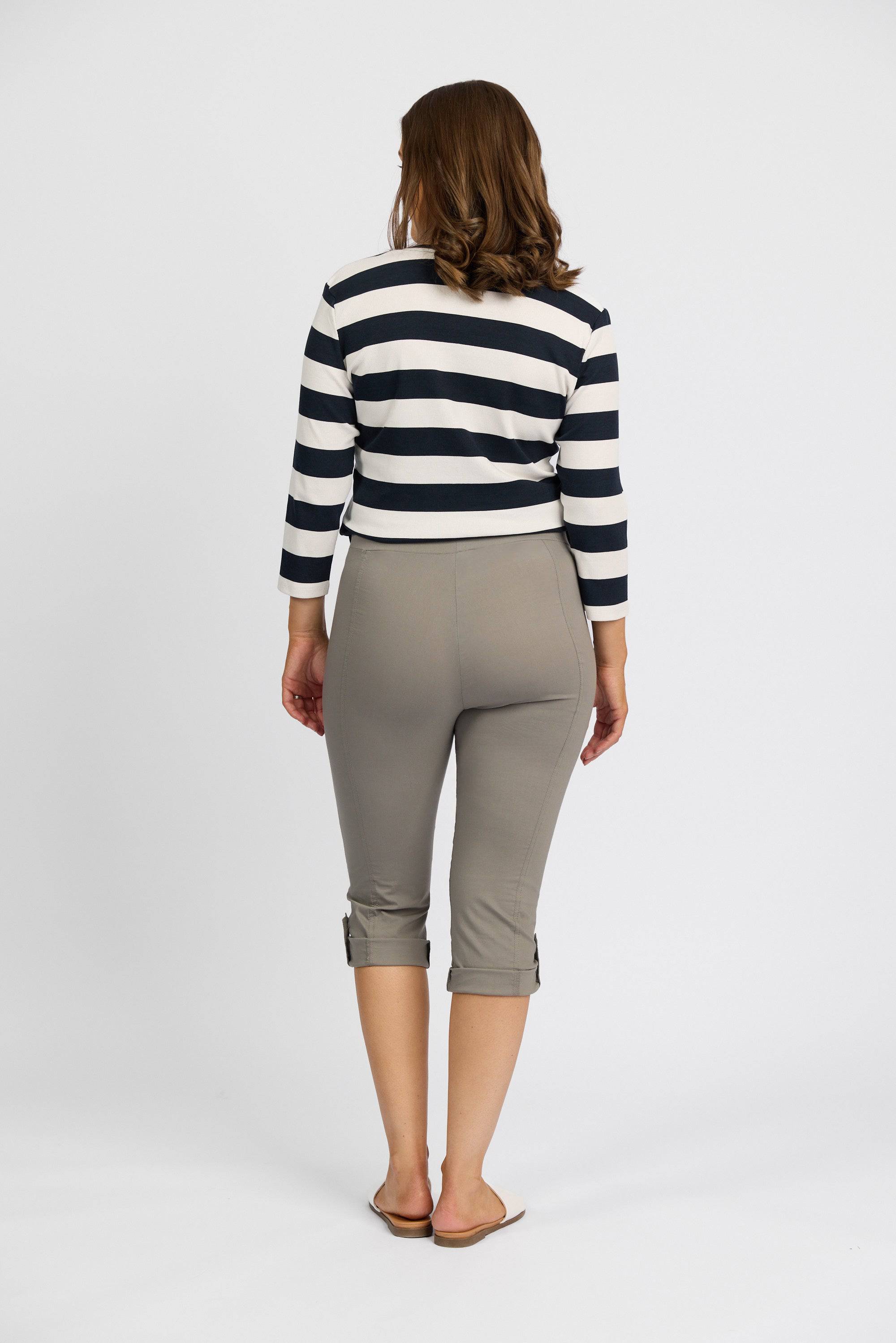 A woman with shoulder-length wavy hair faces away, wearing a black and white striped long-sleeve shirt and Vassalli Paris 3/4 Cargo Short in Latte, set against a plain white background.