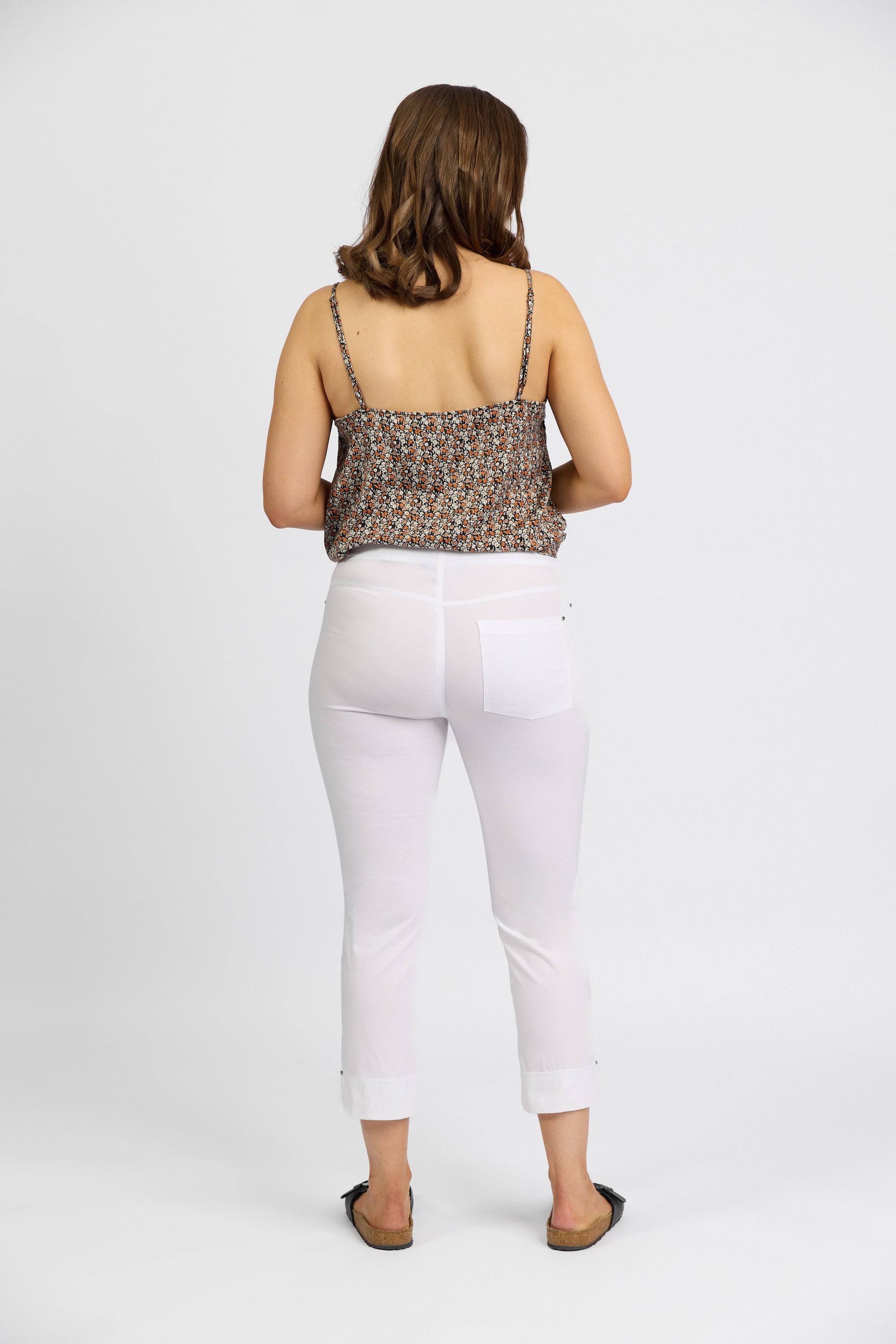 A woman faces away from the camera wearing a Vassalli patterned sleeveless top, Vassalli Paris Tour Capri - White pants, and black sandals, set against a plain white background.