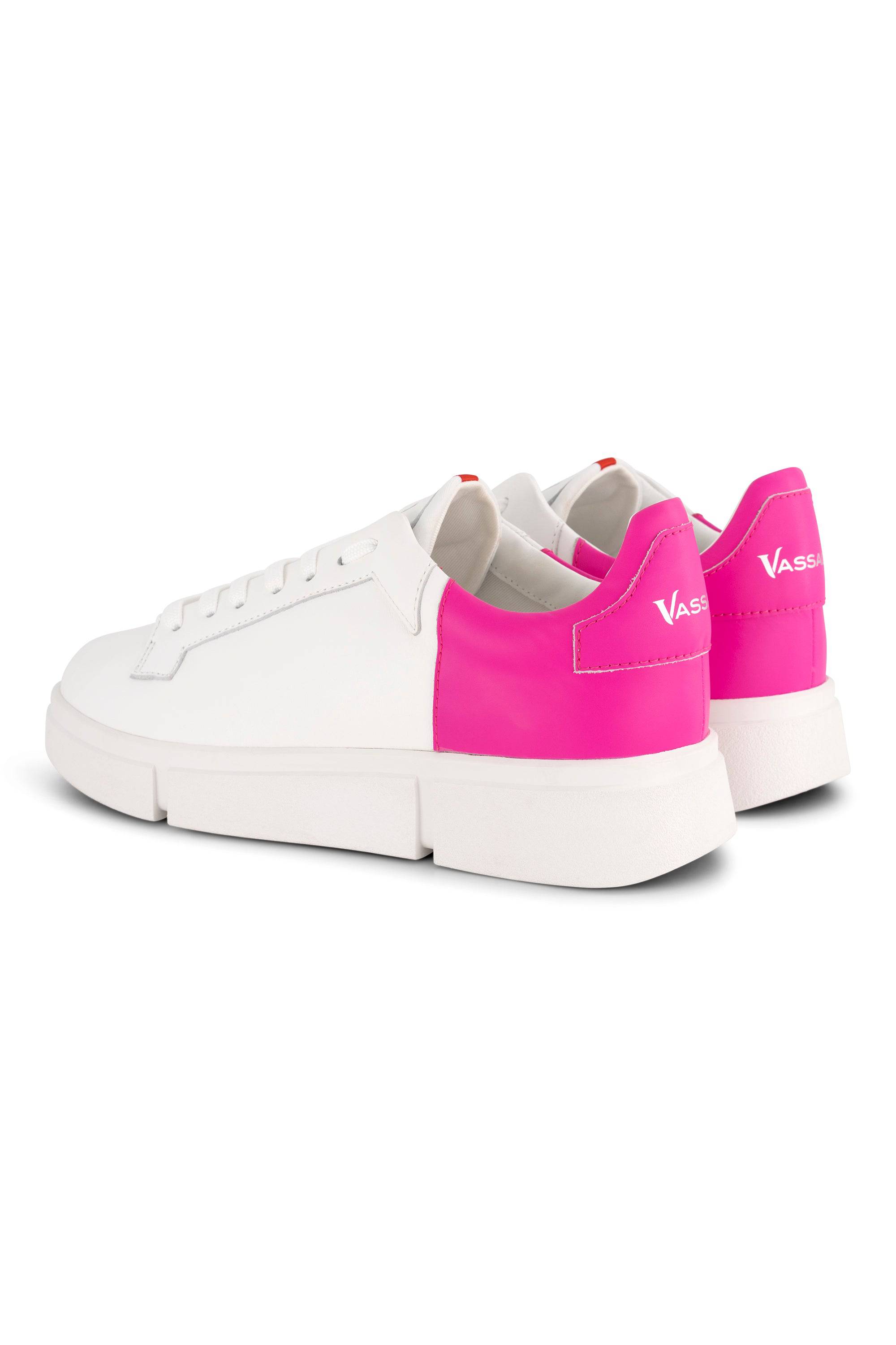 The VS-001 White/Fuchsia Laced Sneaker by Vassalli features a white leather low-top design with bright fuchsia heels, the VASSI logo in white on the back, platform soles, and white laces. Shown from a rear three-quarter angle.