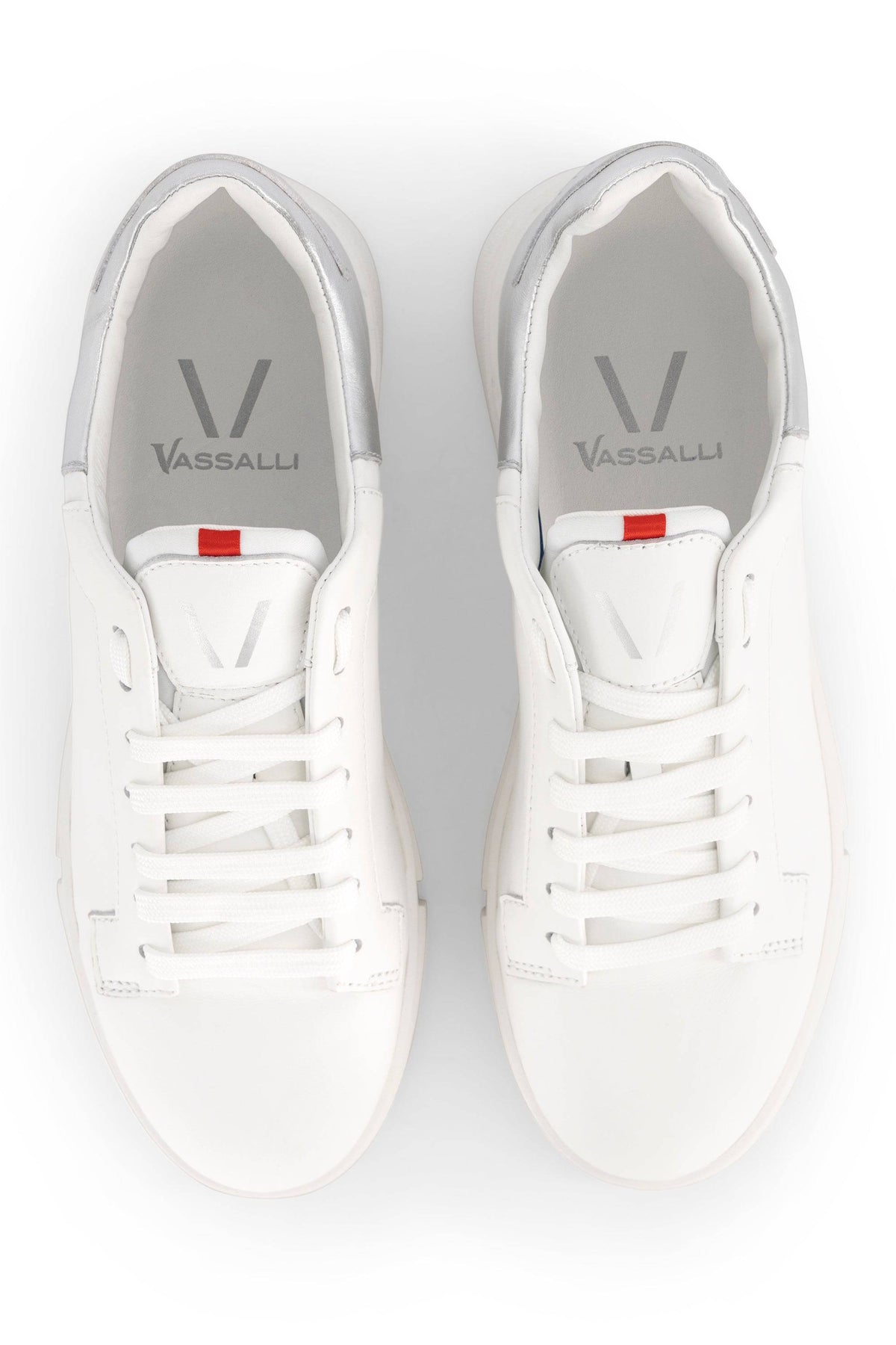 A pair of Vassalli VS-001 White/Silver Laced Sneakers seen from above, with white laces, gray lining, and a small red tab on each tongue.