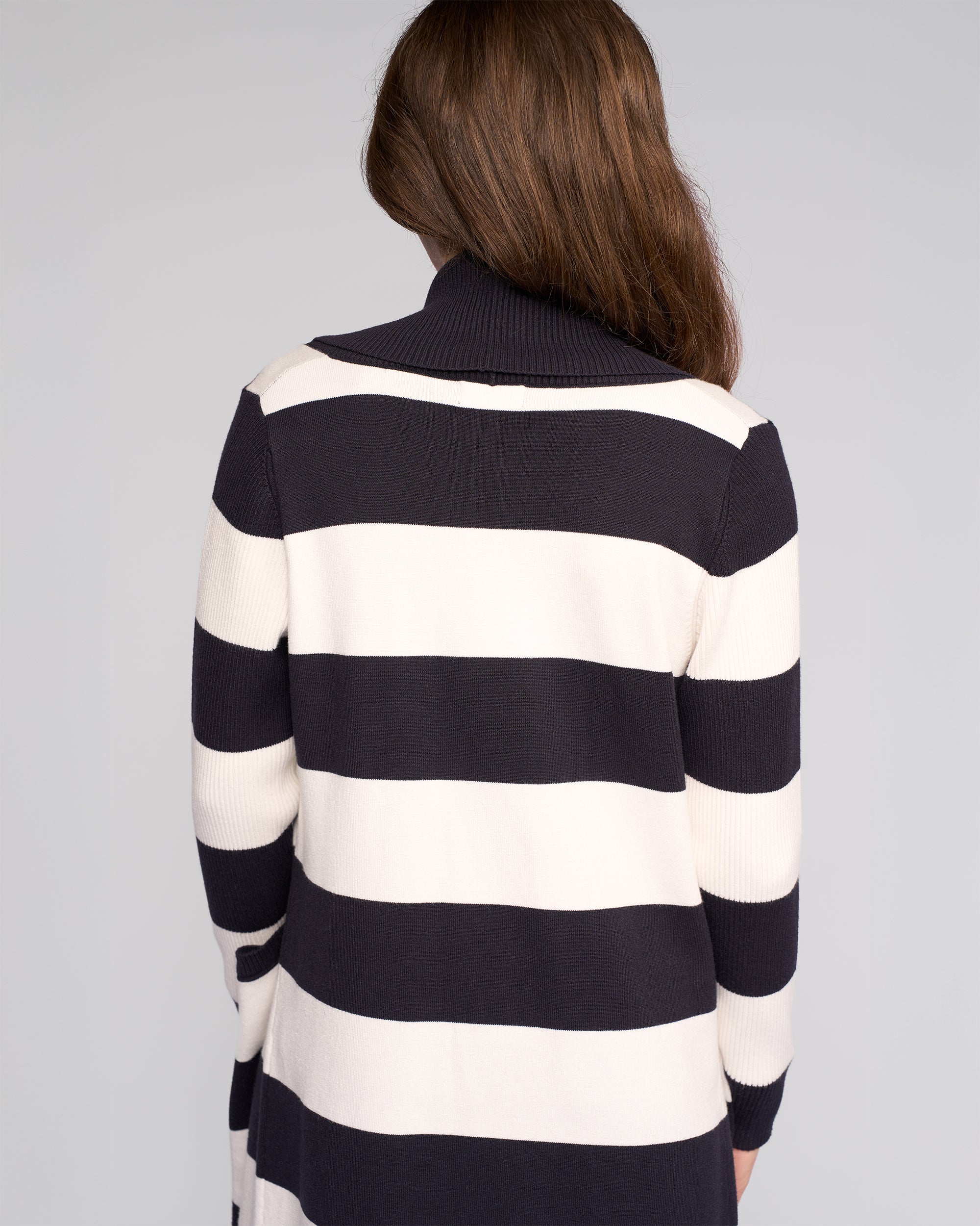 A person with long brown hair, seen from behind, wears the Vassalli Downtown Cardi in Ink/Winter White. This long-sleeved, black and white striped cardigan is shown against a plain light background.