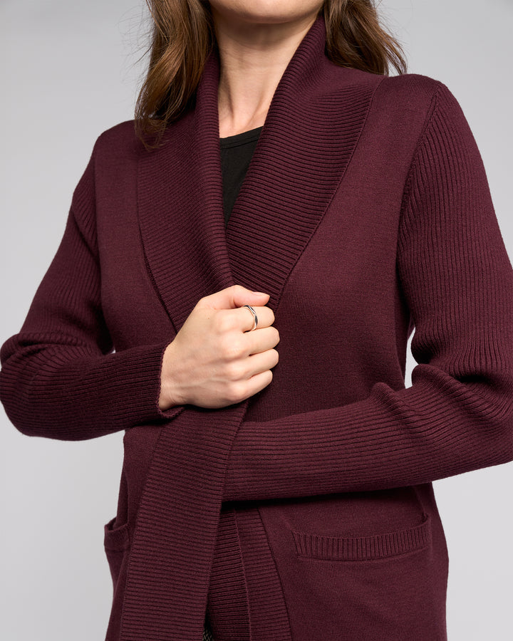 Wearing the Vassalli Downtown Cardi in Merlot over a black top, a person holds the cardigan closed with one hand. Photo is cropped to show torso and part of face.