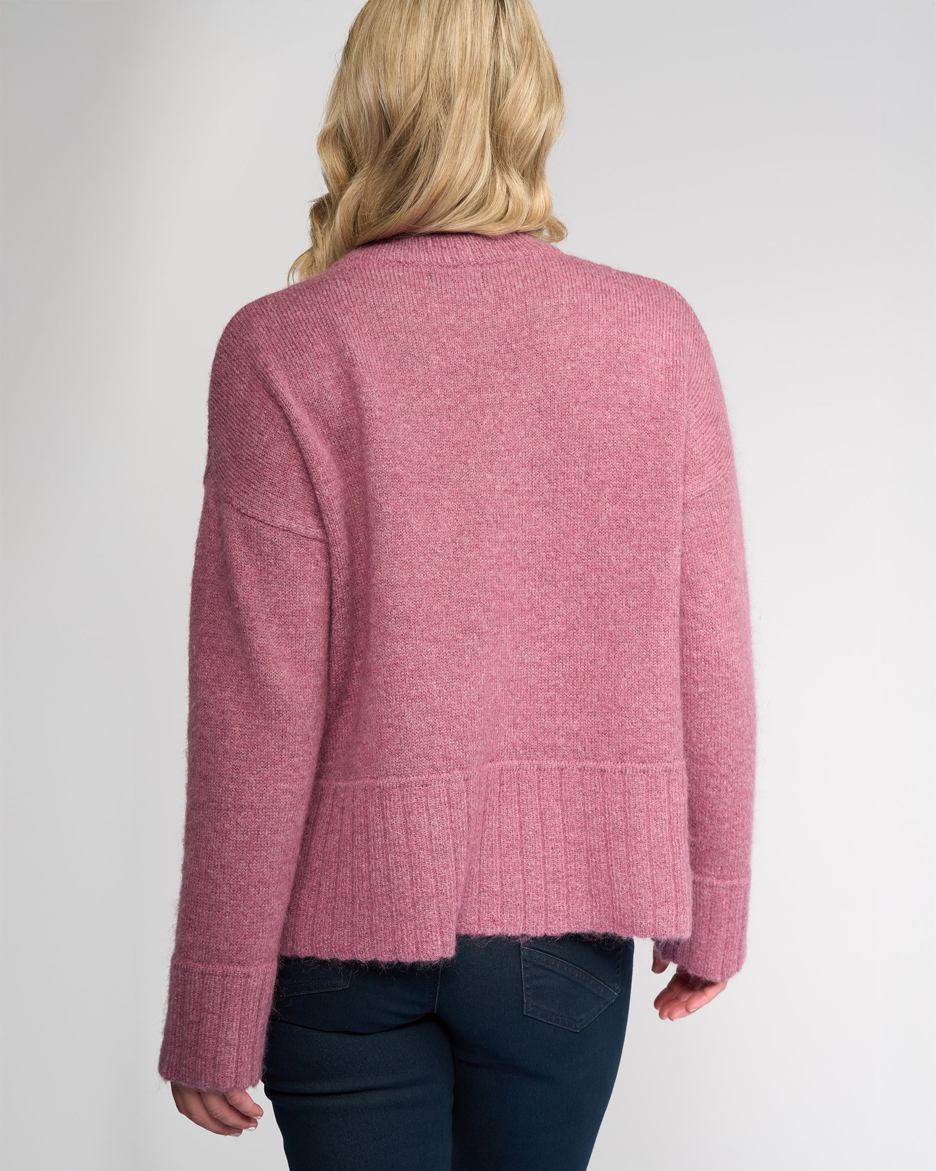 A person with blonde, wavy hair is seen from behind wearing the Vassalli Orbit Sweater - Port, paired with dark blue jeans, set against a plain light background.