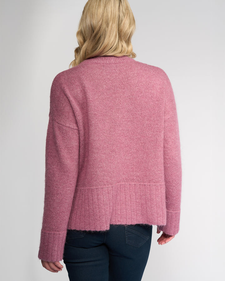 A person with blonde, wavy hair is seen from behind wearing the Vassalli Orbit Sweater - Port, paired with dark blue jeans, set against a plain light background.