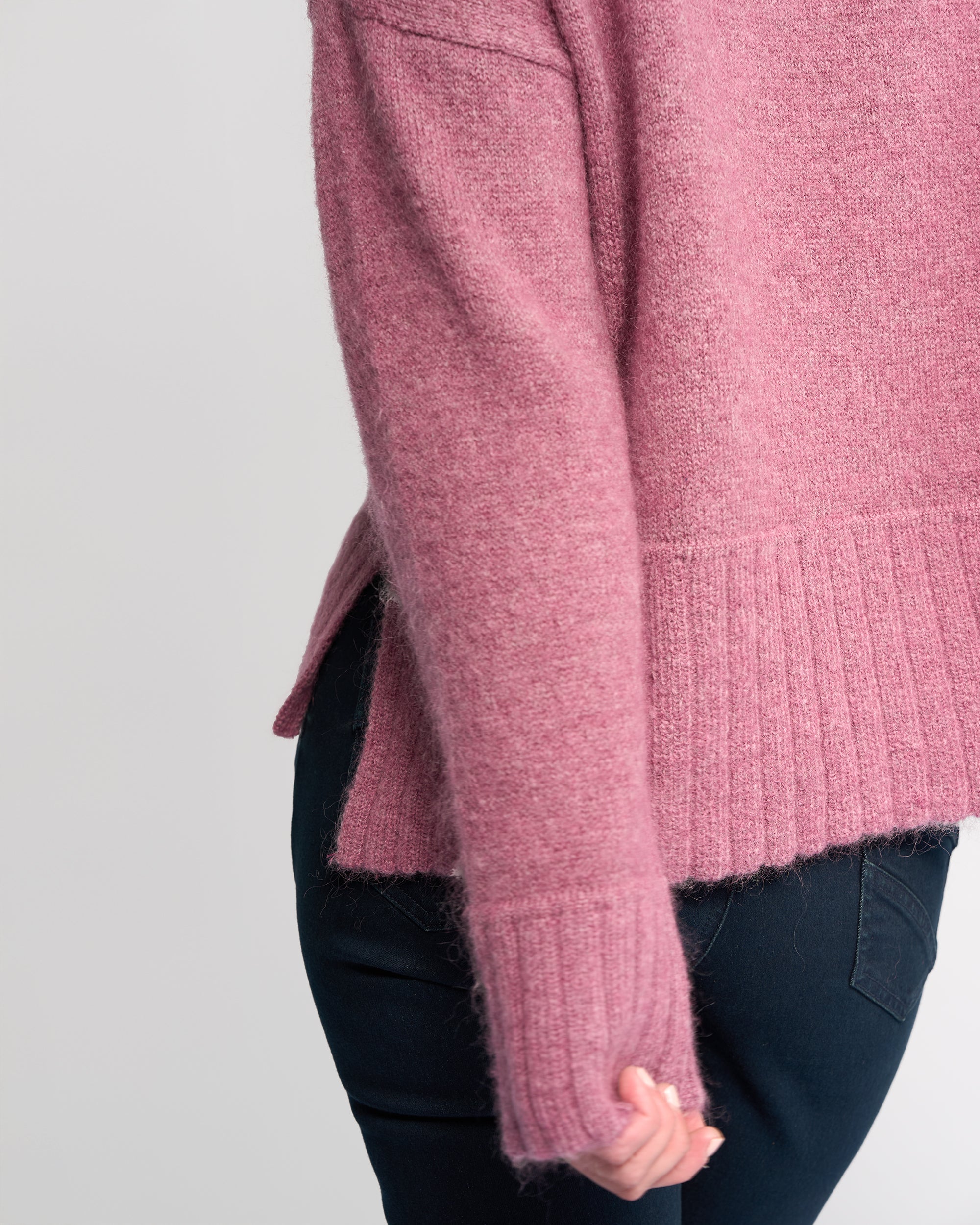 Someone is wearing the Vassalli Orbit Sweater in Port, a soft, relaxed-fit knit with ribbed cuffs and hem. Only their torso and arm are shown against a plain light background, paired with dark pants.