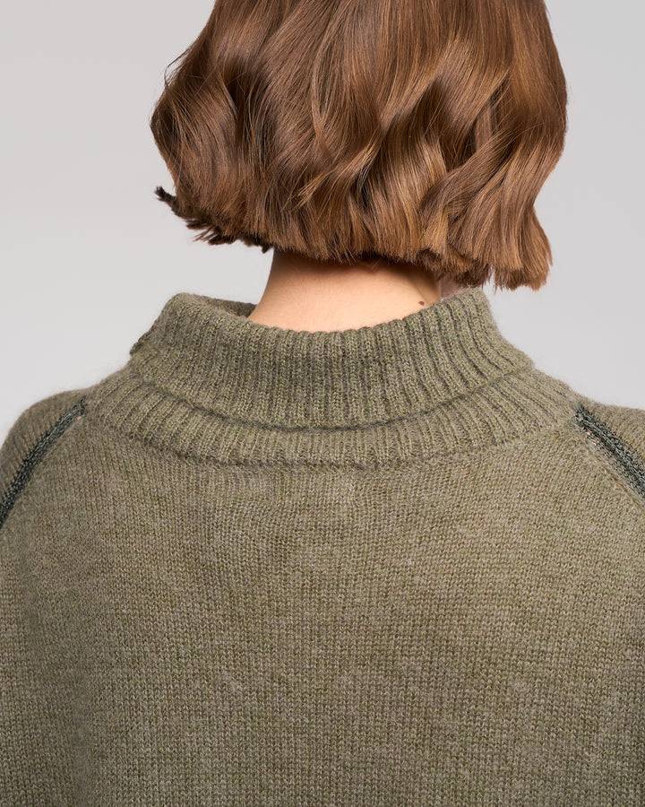 A person with short, wavy brown hair is shown from behind, wearing the Vassalli Mellow Sweater in Elm. The sweater features a ribbed collar and is set against a plain, neutral background.