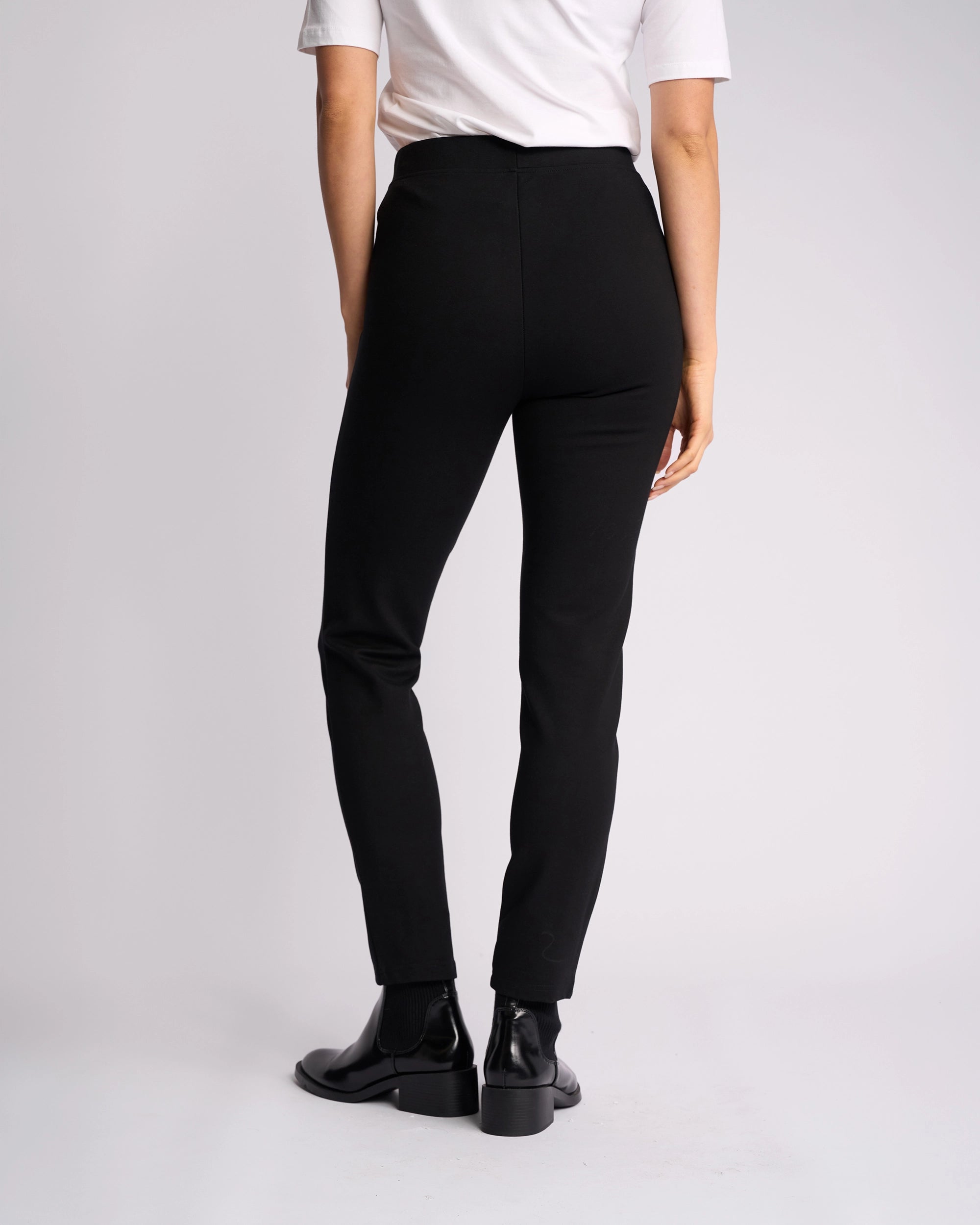 A person stands against a plain light background, shown from the back, wearing a white short-sleeve shirt and Vassalli Fortune Pant - Black.