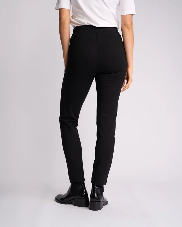 A person stands against a plain light background, shown from the back, wearing a white short-sleeve shirt and Vassalli Fortune Pant - Black.