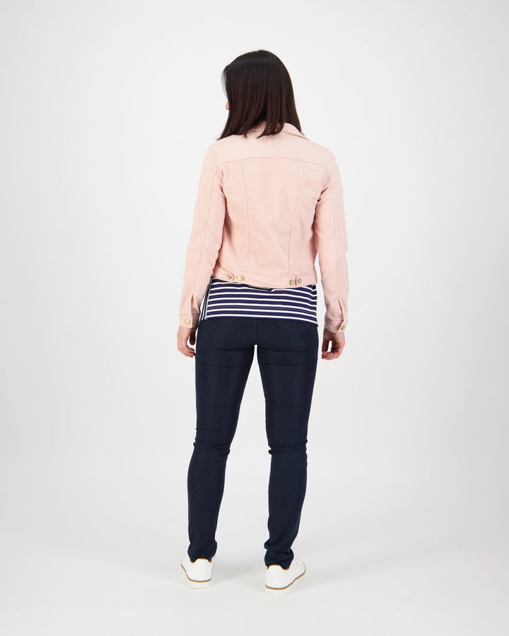 A woman stands facing away from the camera, wearing the Vassalli Sloane Denim Jacket in French Rose, a navy and white striped shirt, dark skinny jeans, and white shoes against a plain white background.