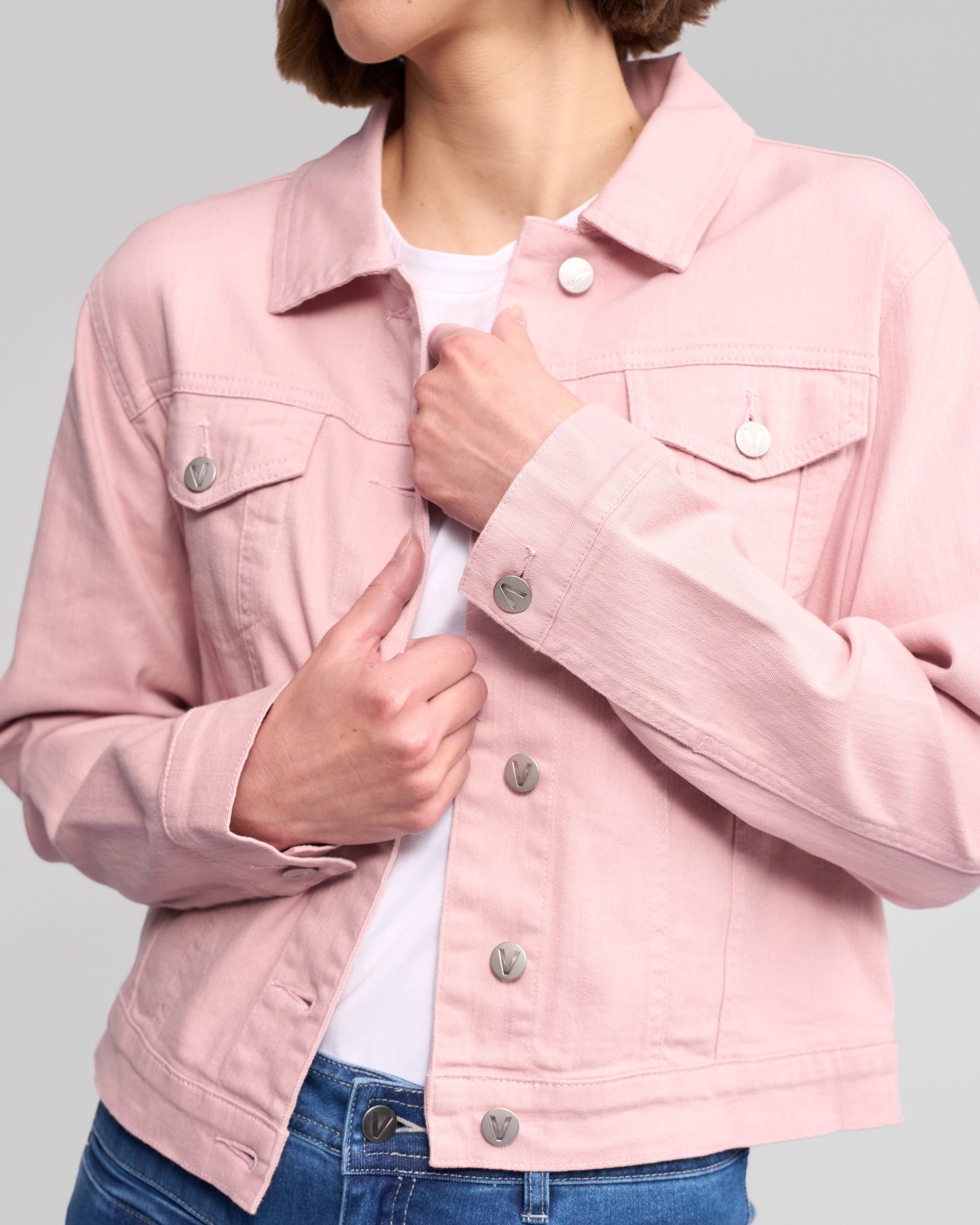 A person, head partially out of frame, buttons up the Vassalli Ratio Jacket - French Rose Denim over a white shirt and blue jeans, set against a plain gray background.