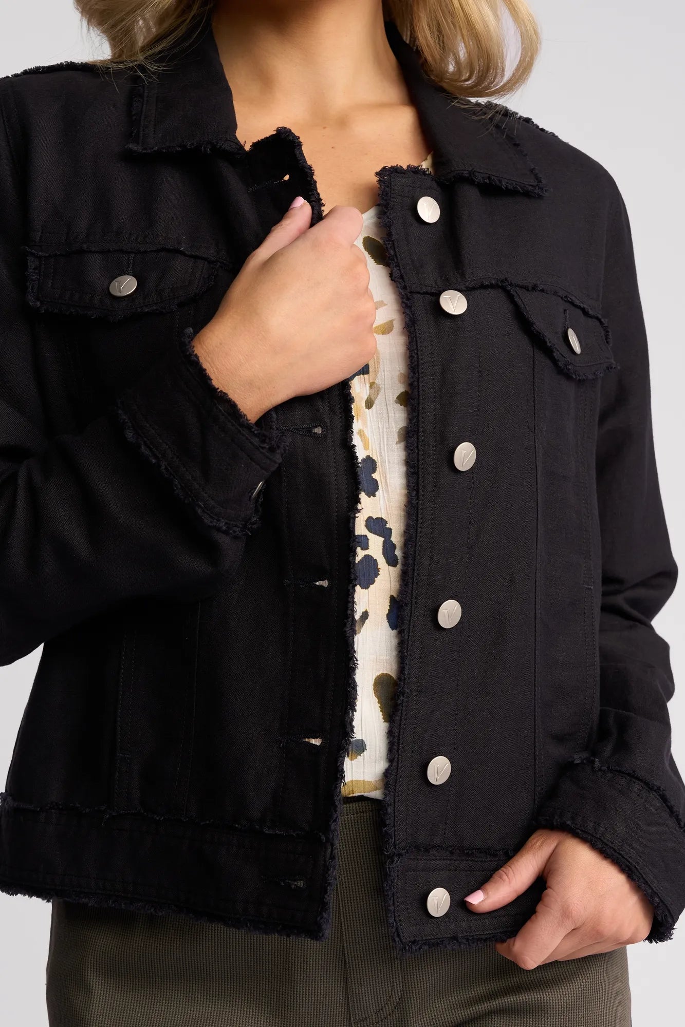 A person wears a navy Vassalli Aura Jacket over a floral top, with one hand adjusting the collar and the other resting near the waist.