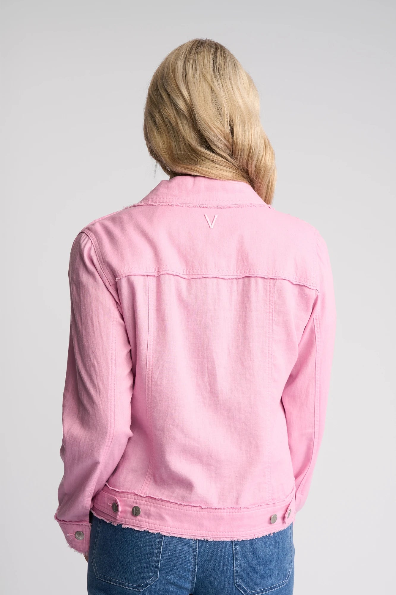 A person with long blonde hair wearing a Vassalli Aura Jacket - Taffy and blue jeans, shown from the back against a plain light gray background.