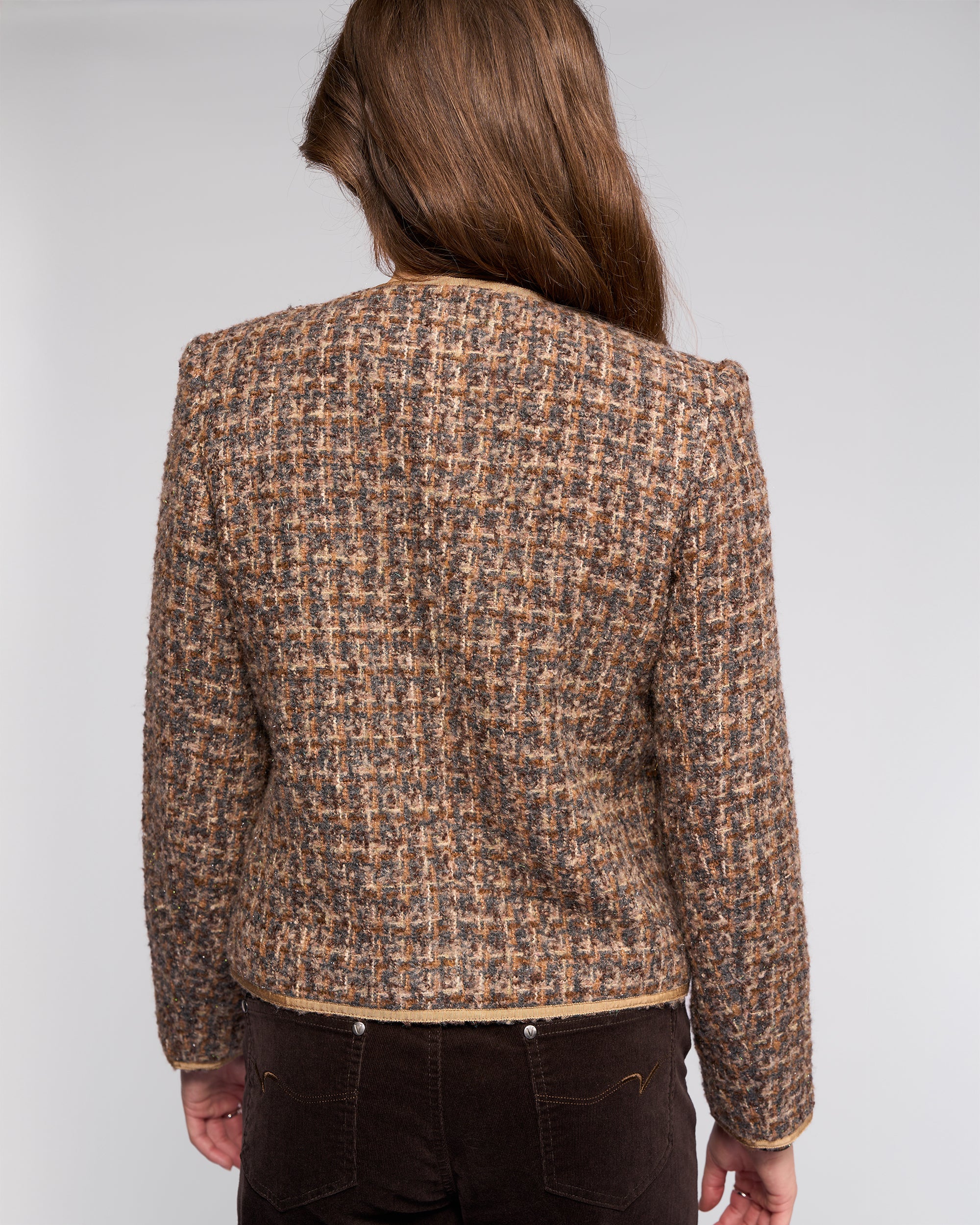 A person with long brown hair, seen from behind, wears the Vassalli Stage Jacket - Florence in a brown and beige plaid pattern, paired with dark brown pants against a plain light background.