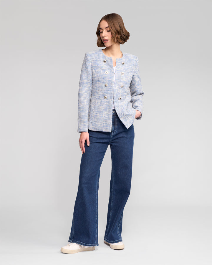 A woman with short brown hair models the Vassalli Lena Jacket - Valli, paired with dark blue wide-leg jeans and white sneakers, against a plain light gray background.