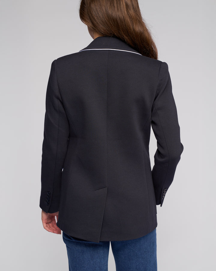 A person with long brown hair, shown from behind against a plain light background, is wearing the Vassalli Ora Blazer - Ink and blue jeans.