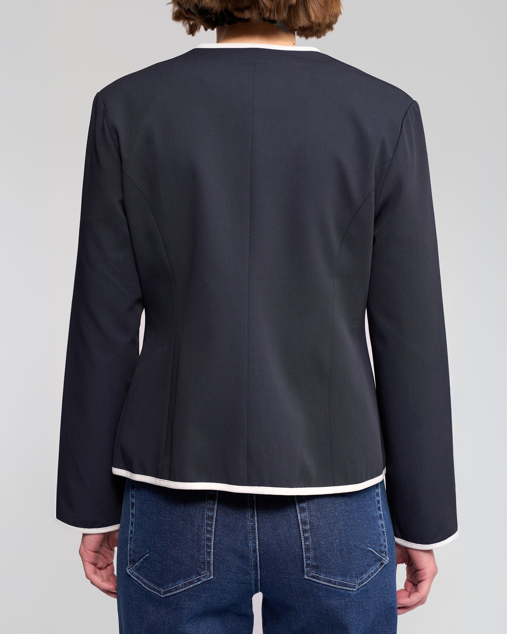 A person is seen from behind wearing the Vassalli Pier Jacket in Ink/White with blue jeans, set against a plain light gray background, showcasing its streamlined silhouette.