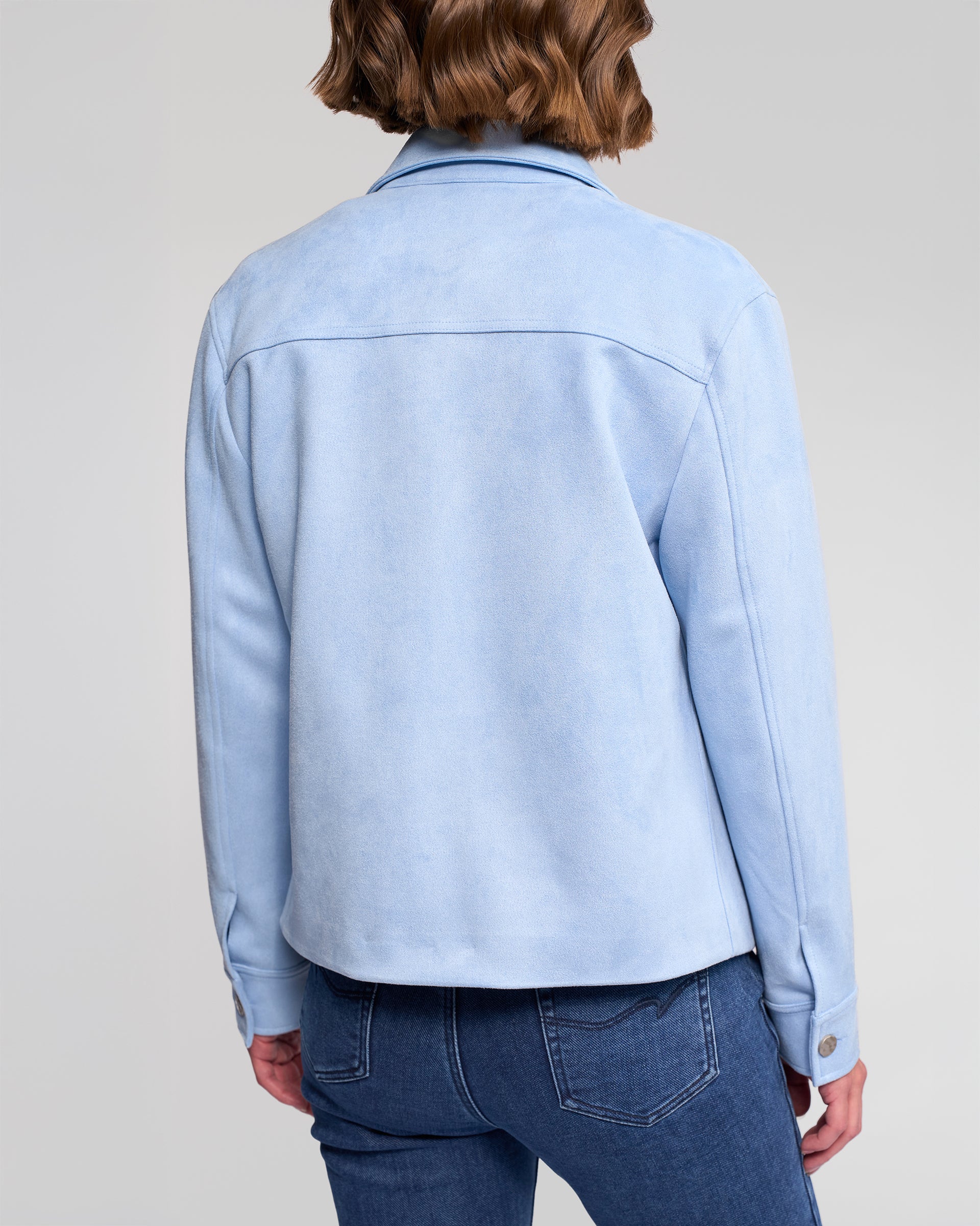 A person with short, wavy brown hair is seen from behind wearing the Vassalli Guest Jacket in Sky Blue with blue jeans, set against a plain light gray background.